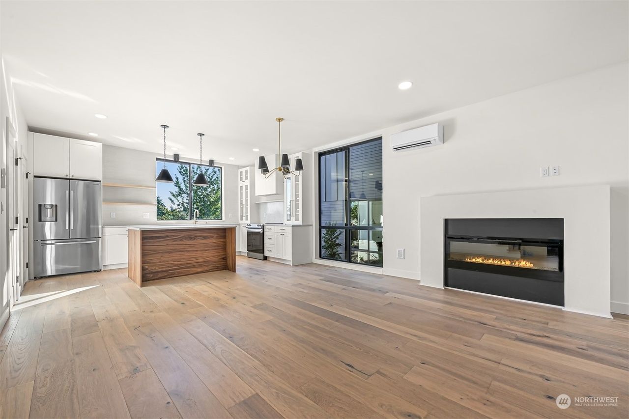 Bright modern open-plan kitchen and living room with wood floors, island, large windows, and a fireplace.