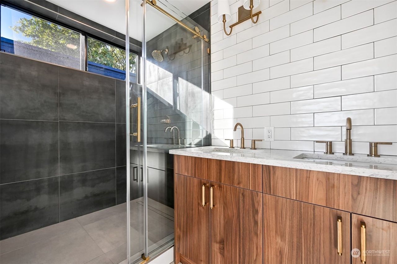 Modern bathroom with glass shower, dark tile wall, and wood vanity with double sinks