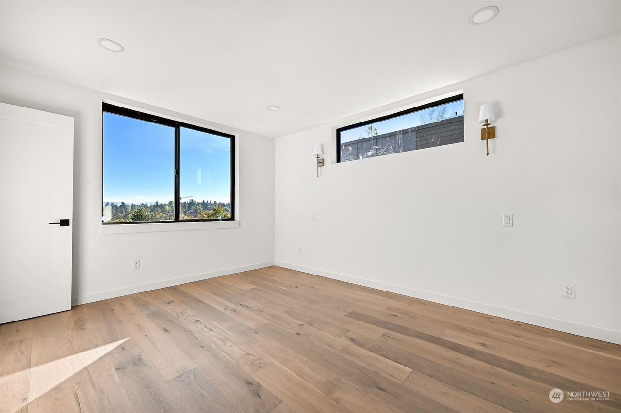 Bright empty room with wood floors, white walls, and large windows overlooking a distant city view