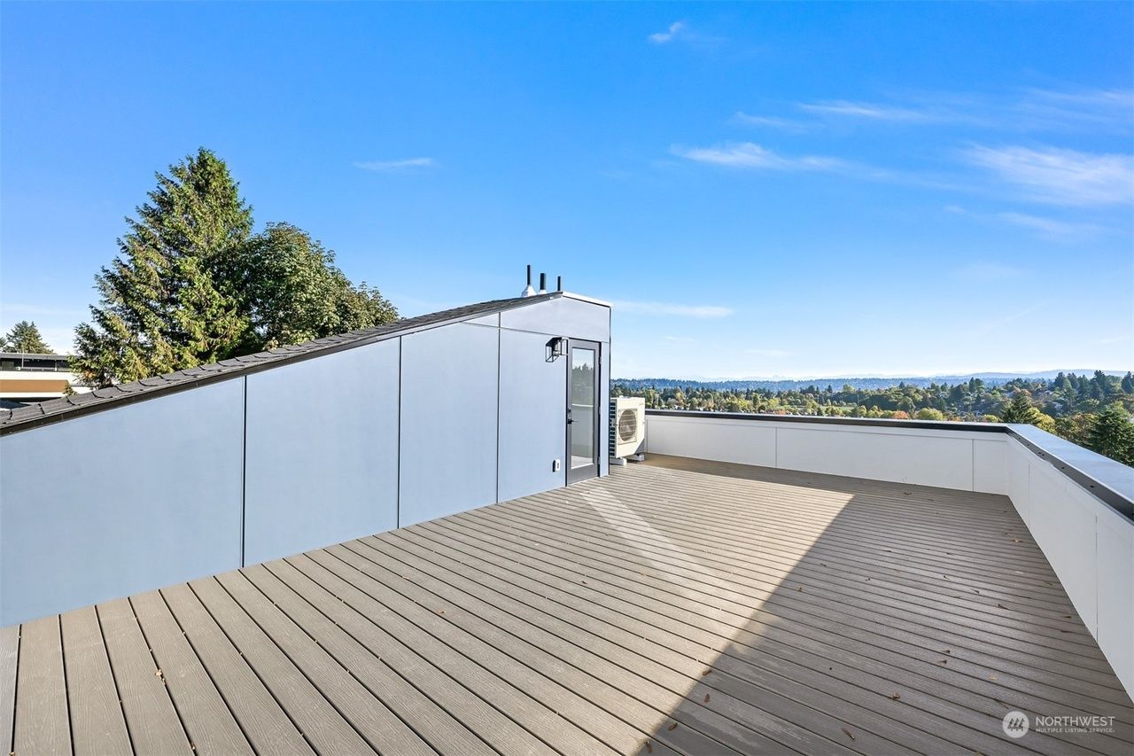 Rooftop deck with light gray siding and wood floor, overlooking a distant landscape under a blue sky