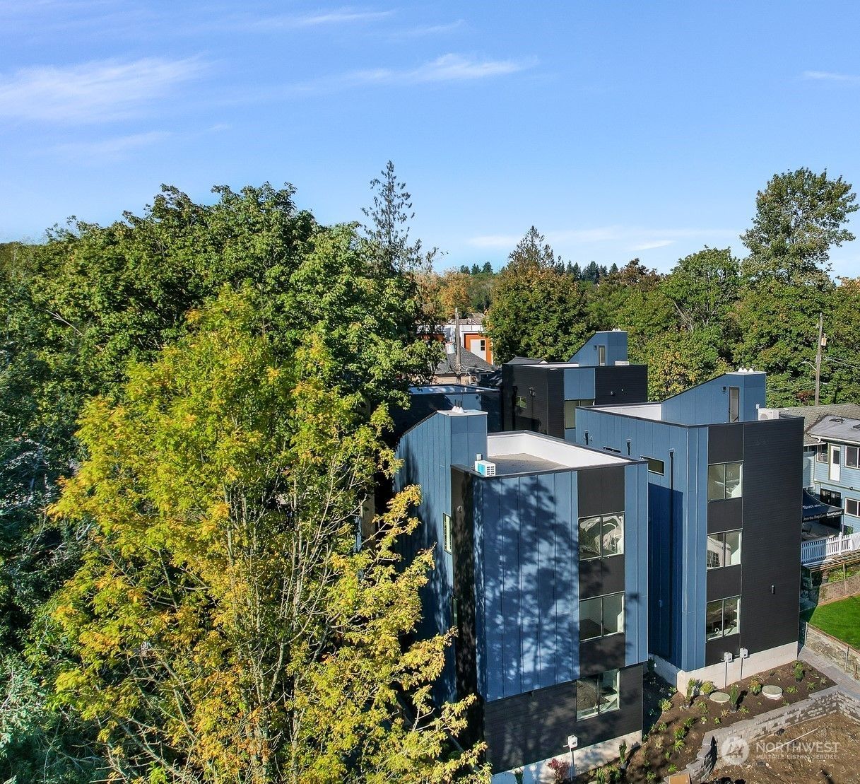 Aerial view of modern apartment buildings surrounded by dense green trees under a blue sky