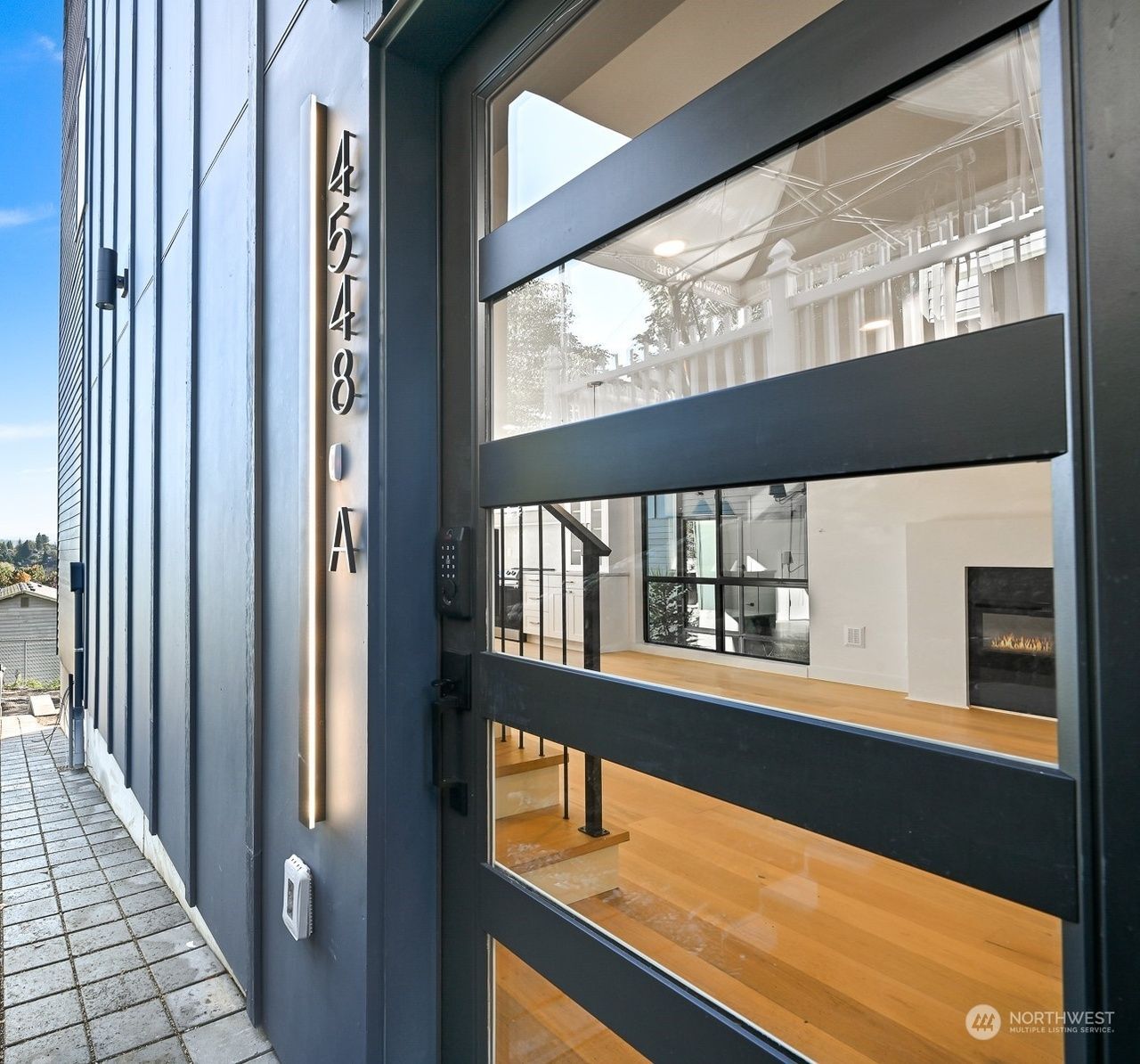 Modern building exterior with glass entry and visible lobby interior, featuring dark metal siding and wood flooring.