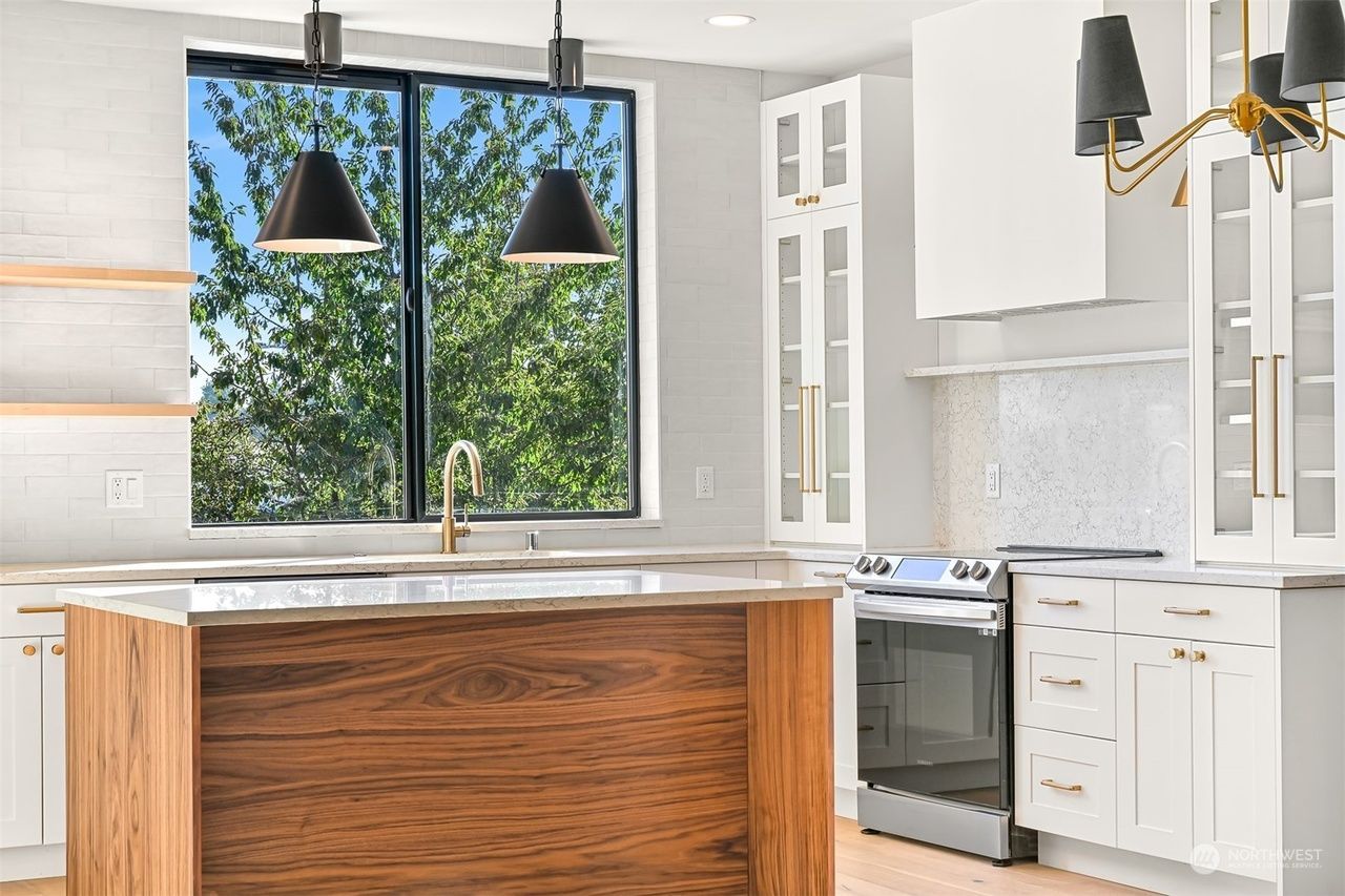 Modern kitchen with wood island, white cabinets, stainless stove, and large window above the sink