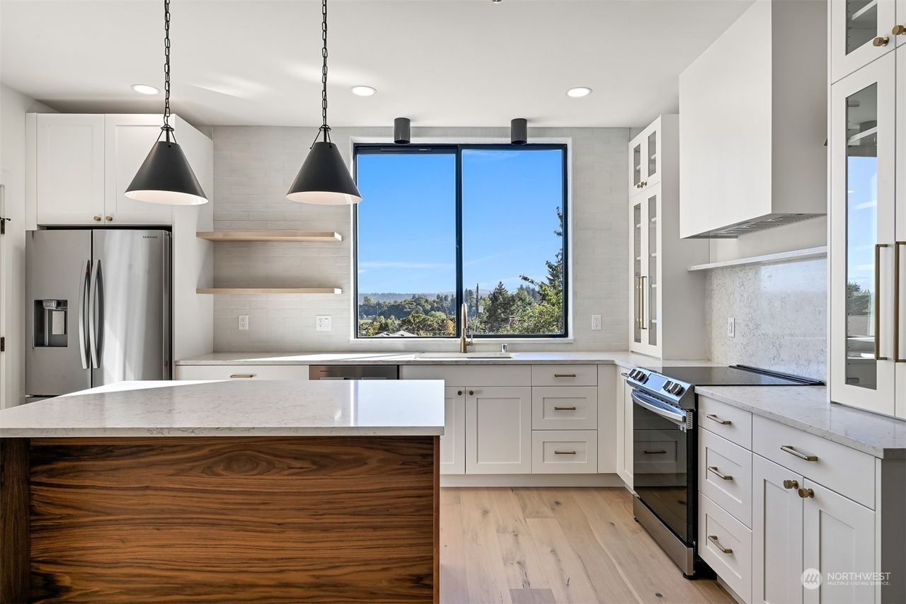 Bright modern kitchen with white cabinets, wood island, pendant lights, and a window view of blue sky and trees