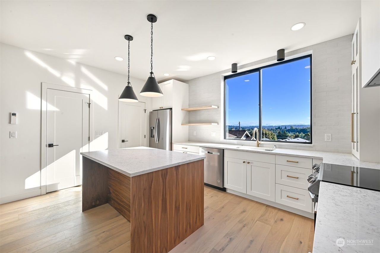 Bright modern kitchen with white cabinets, wood island, and large window overlooking a city view.