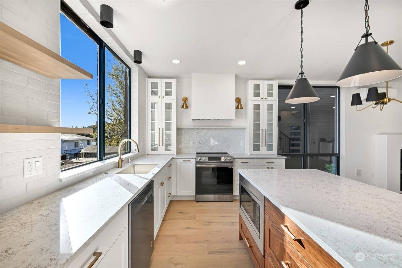 Bright modern kitchen with white cabinets, large windows, island, and black pendant lights