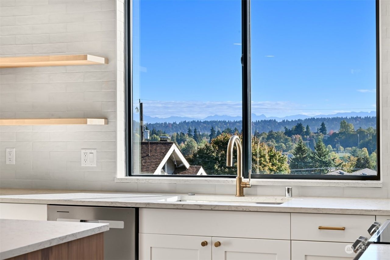 Modern kitchen sink below a large window overlooking trees and distant hills