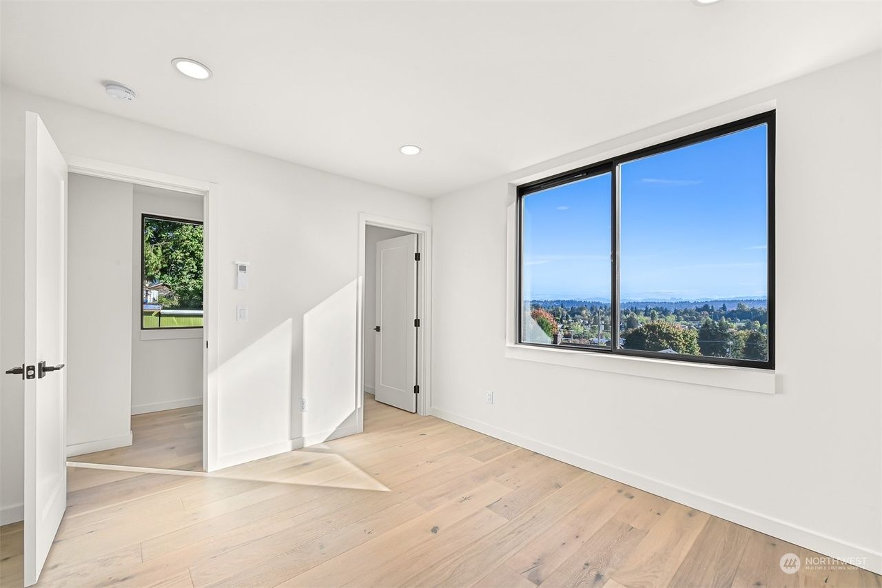 Bright empty room with light wood floors, white walls, and a large window overlooking a city view