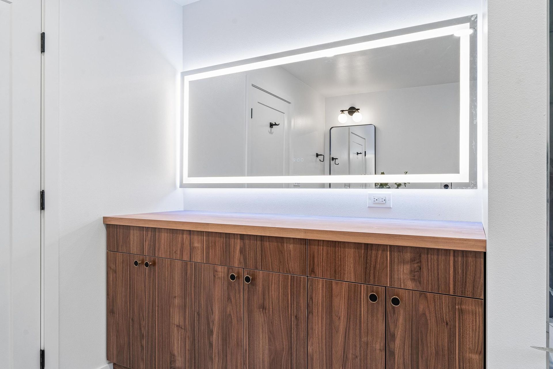 White bathroom vanity with wood cabinets and illuminated mirror