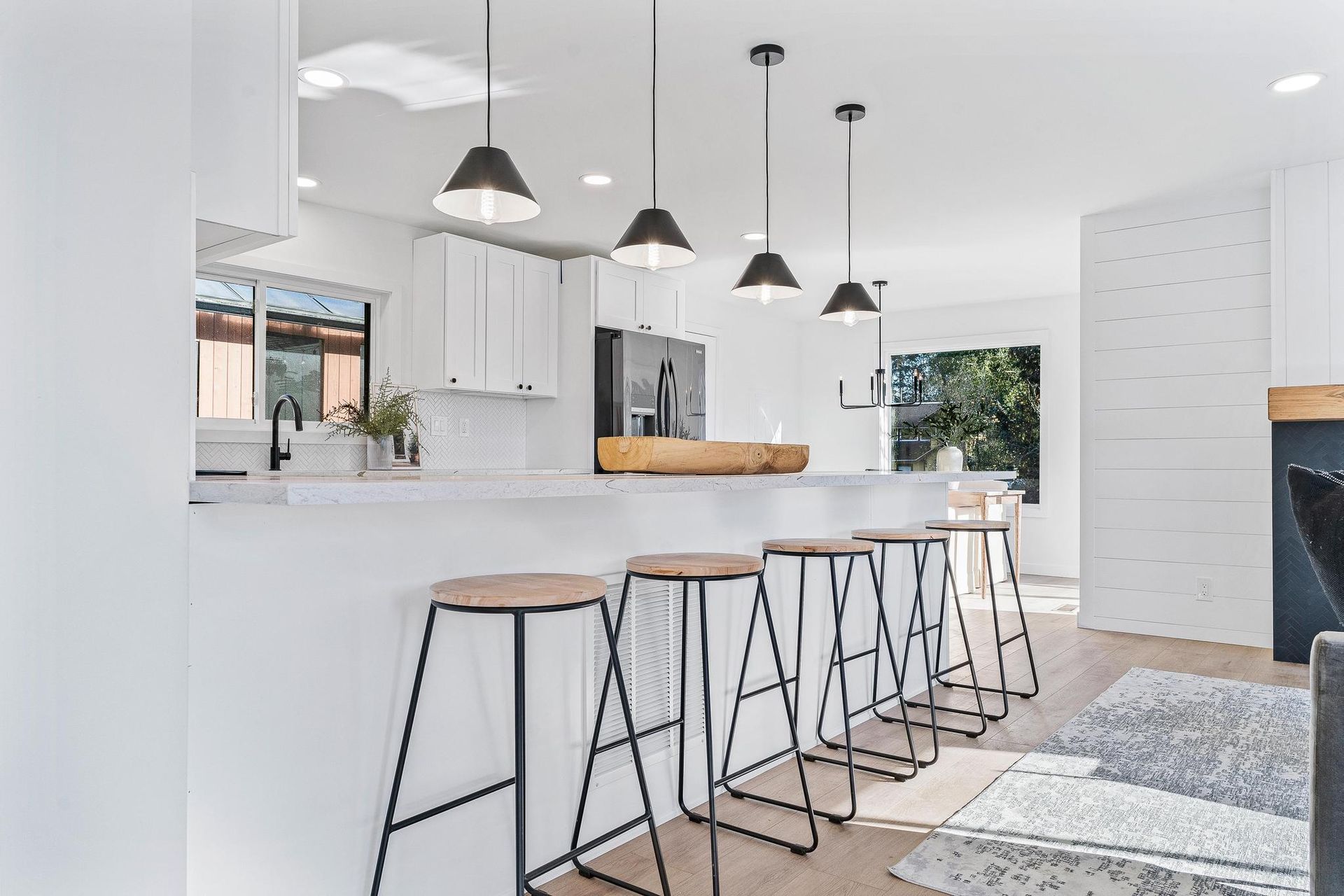 Bright modern kitchen with white island, black stools, pendant lights, and wood accents.