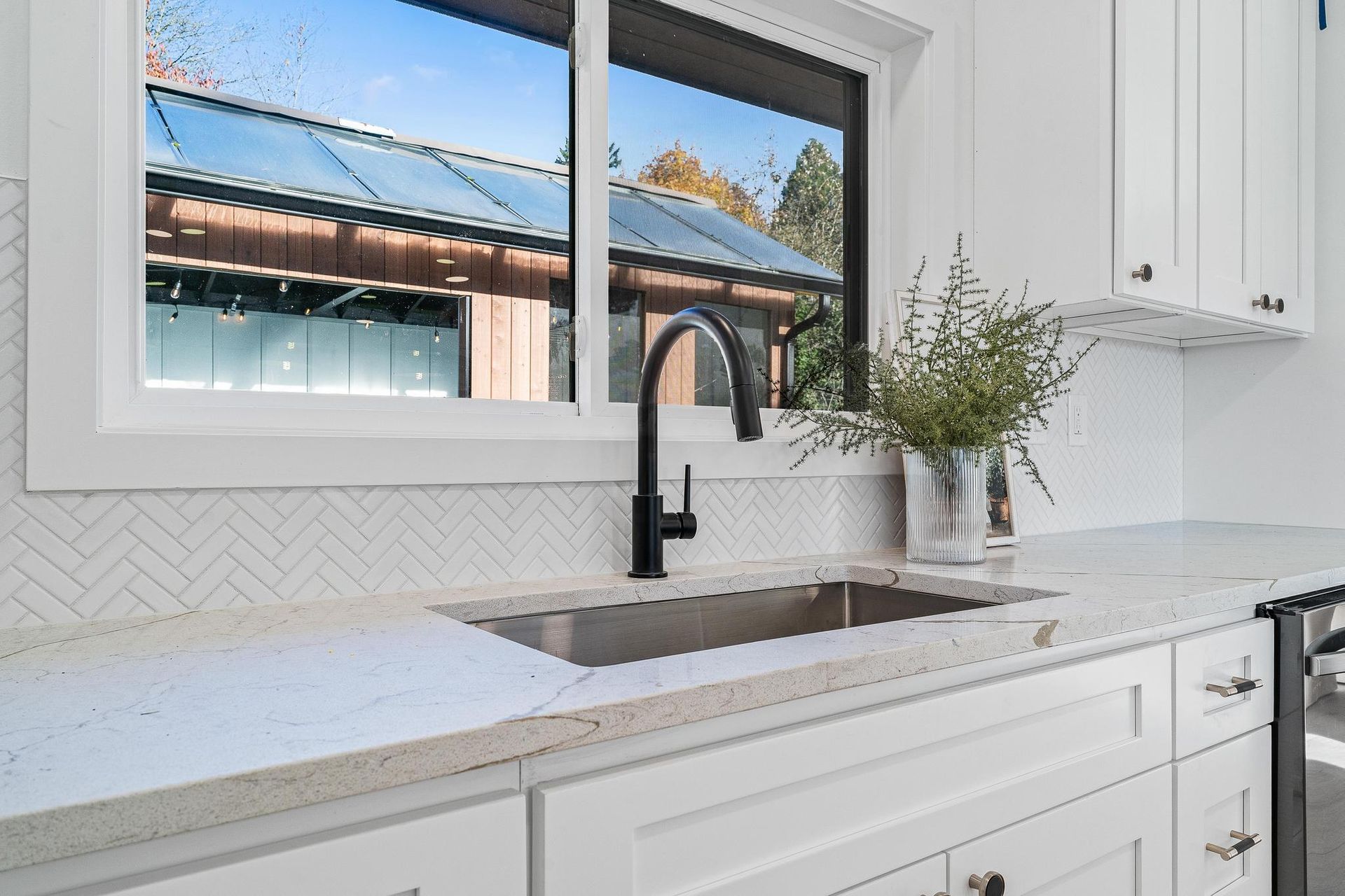 Bright white kitchen with black faucet, marble countertop, window, and vase of greenery