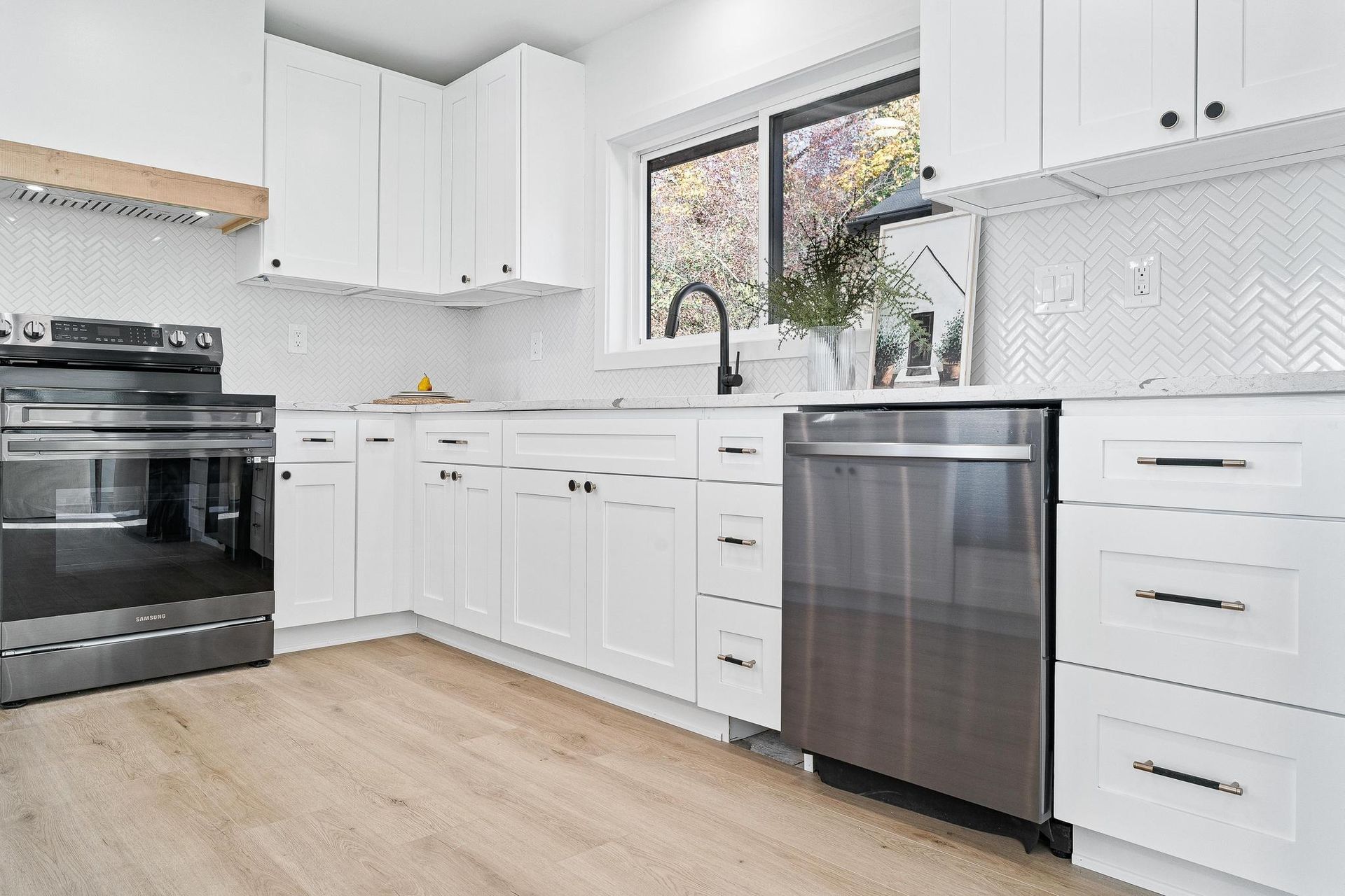 Modern white kitchen with black stove, stainless dishwasher, and large window above sink