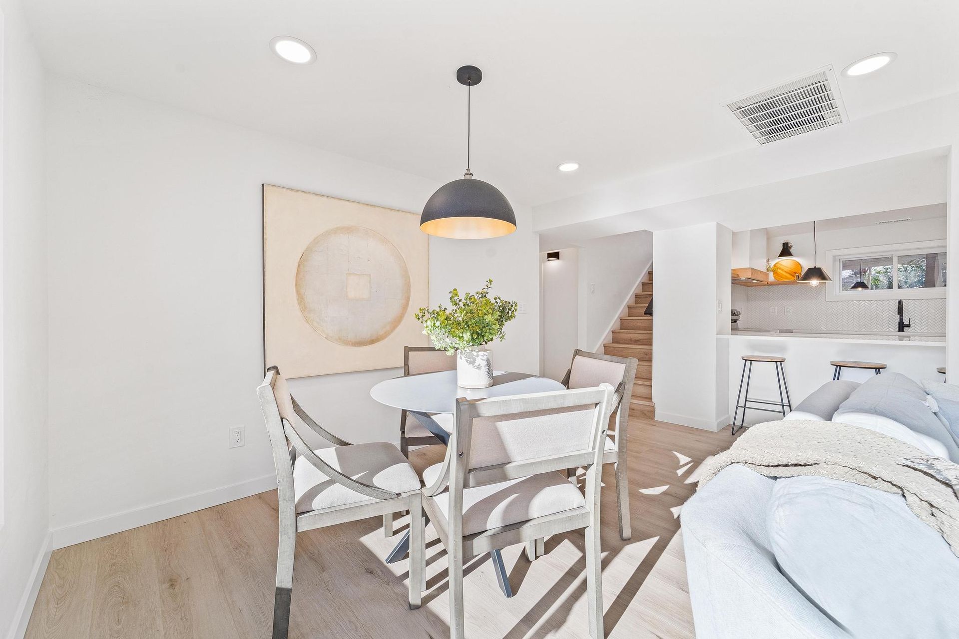 Bright open dining area with glass table, white chairs, pendant light, and adjacent bedroom nook