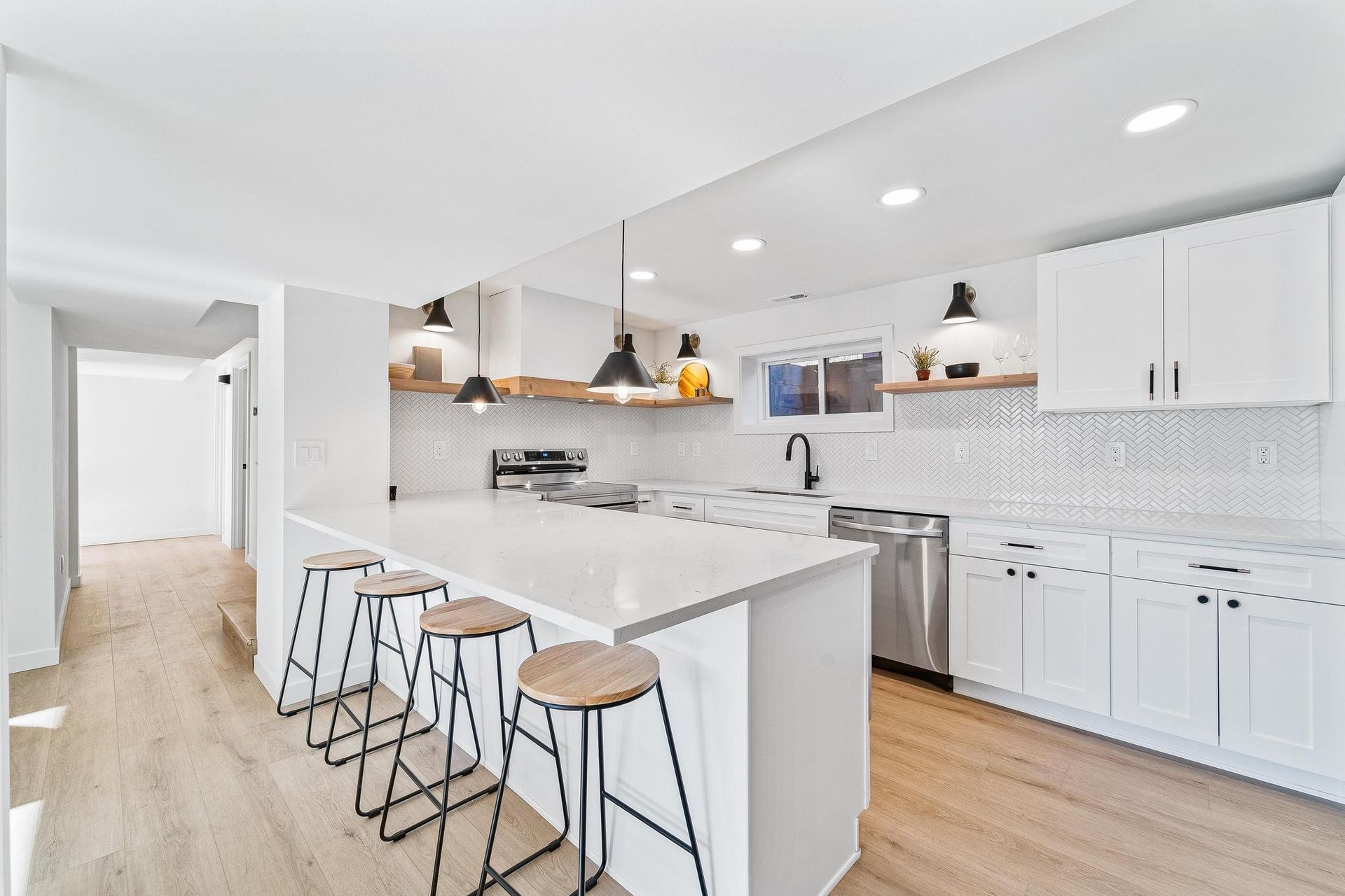 Bright modern kitchen with white cabinets, marble island, bar stools, and wood floors