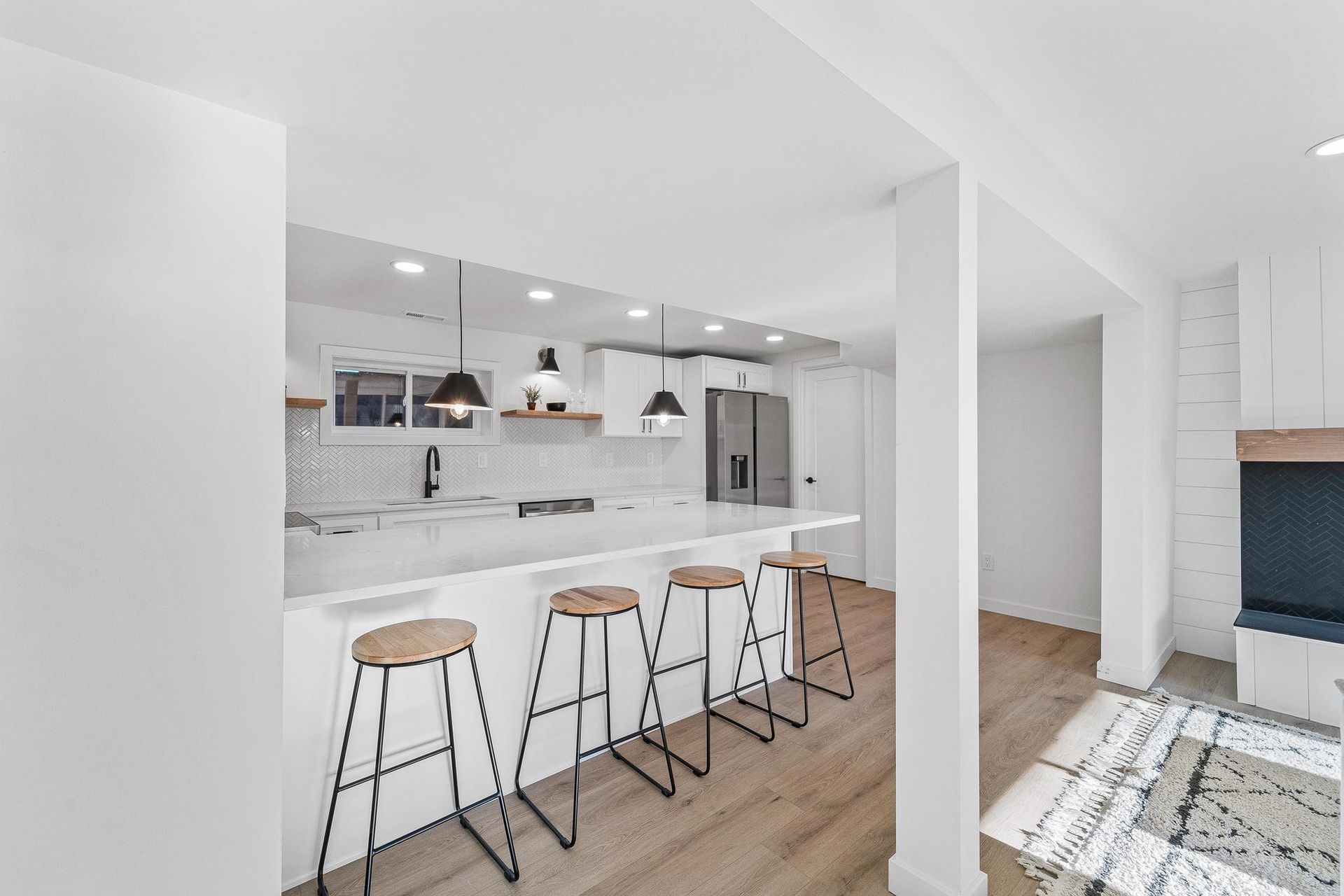 Bright modern kitchen with white cabinetry, wood stools, and hardwood floors