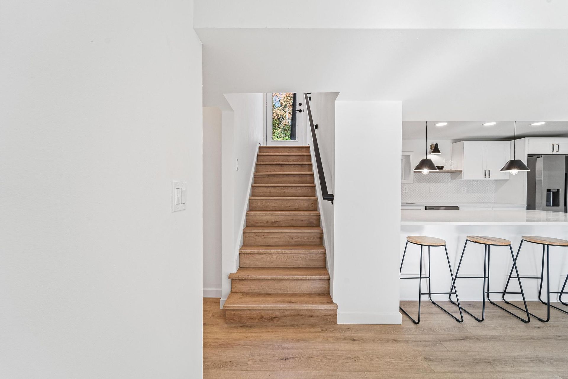 Bright modern interior with a wooden staircase leading upstairs beside a white kitchen island and stools
