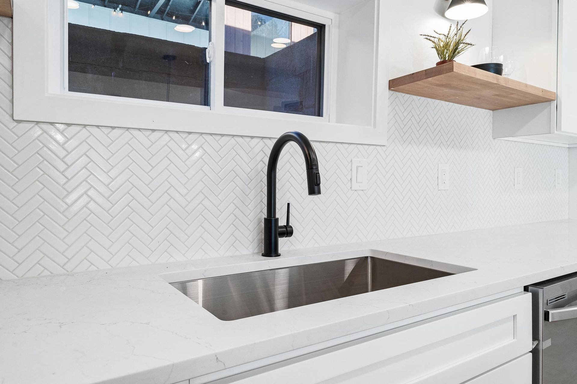 Modern white kitchen countertop with stainless sink, black faucet, and herringbone tile backsplash