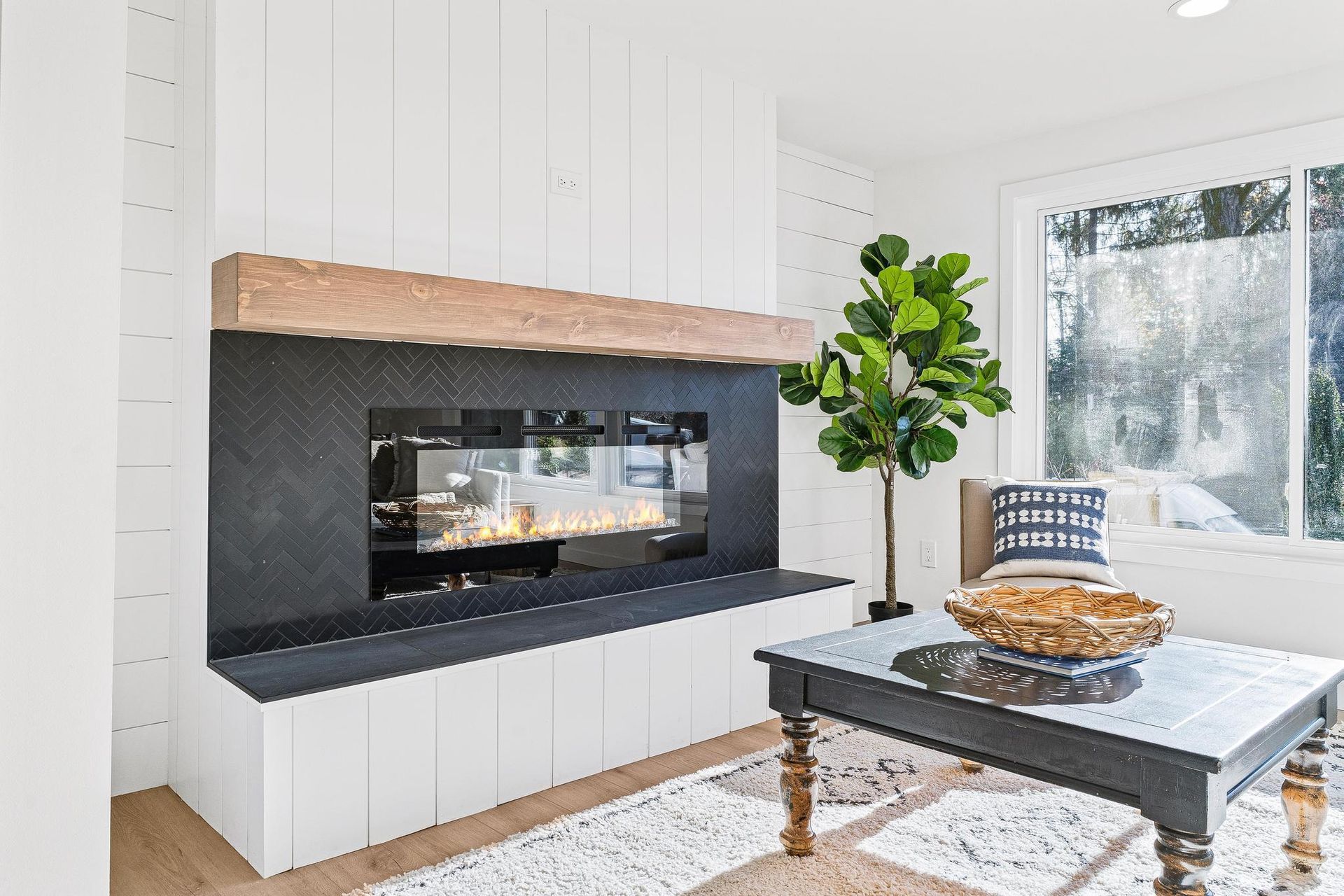 Modern living room with white shiplap walls, black fireplace, coffee table, plant, and large window
