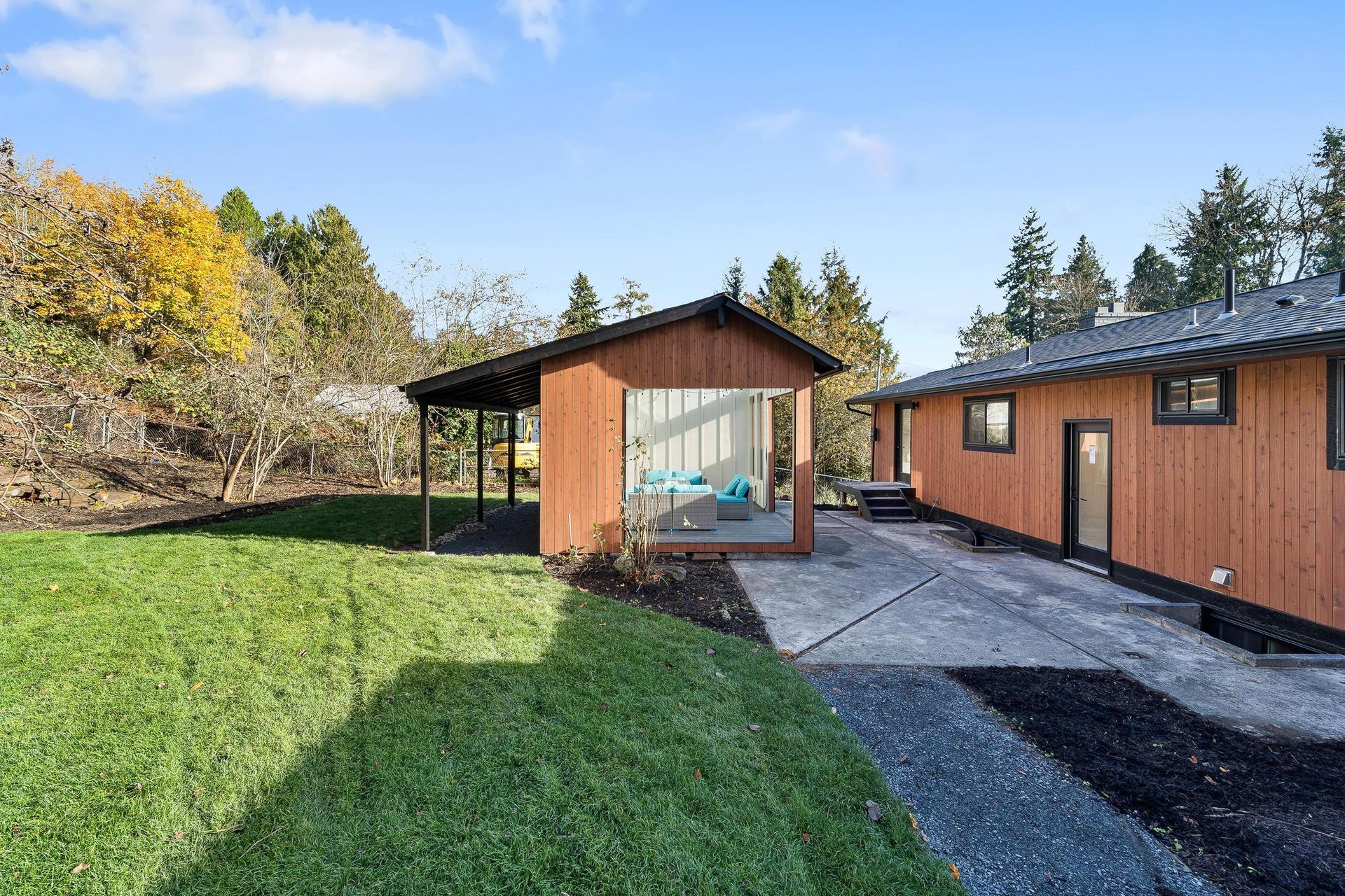 Modern wooden house with covered patio, gravel path, and green lawn in a sunny yard