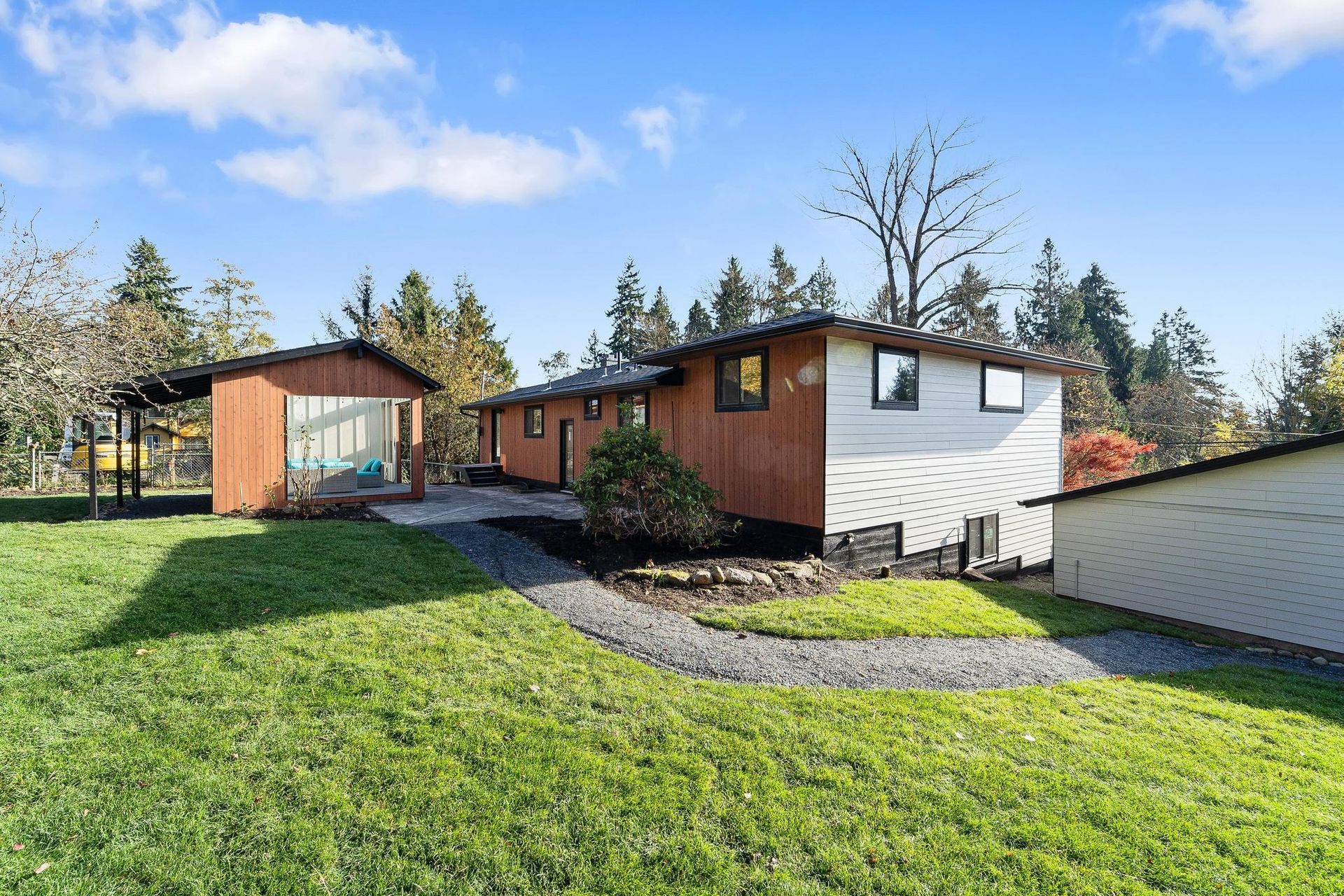 Modern house with white and wood exterior, green lawn, and a paved driveway under a blue sky