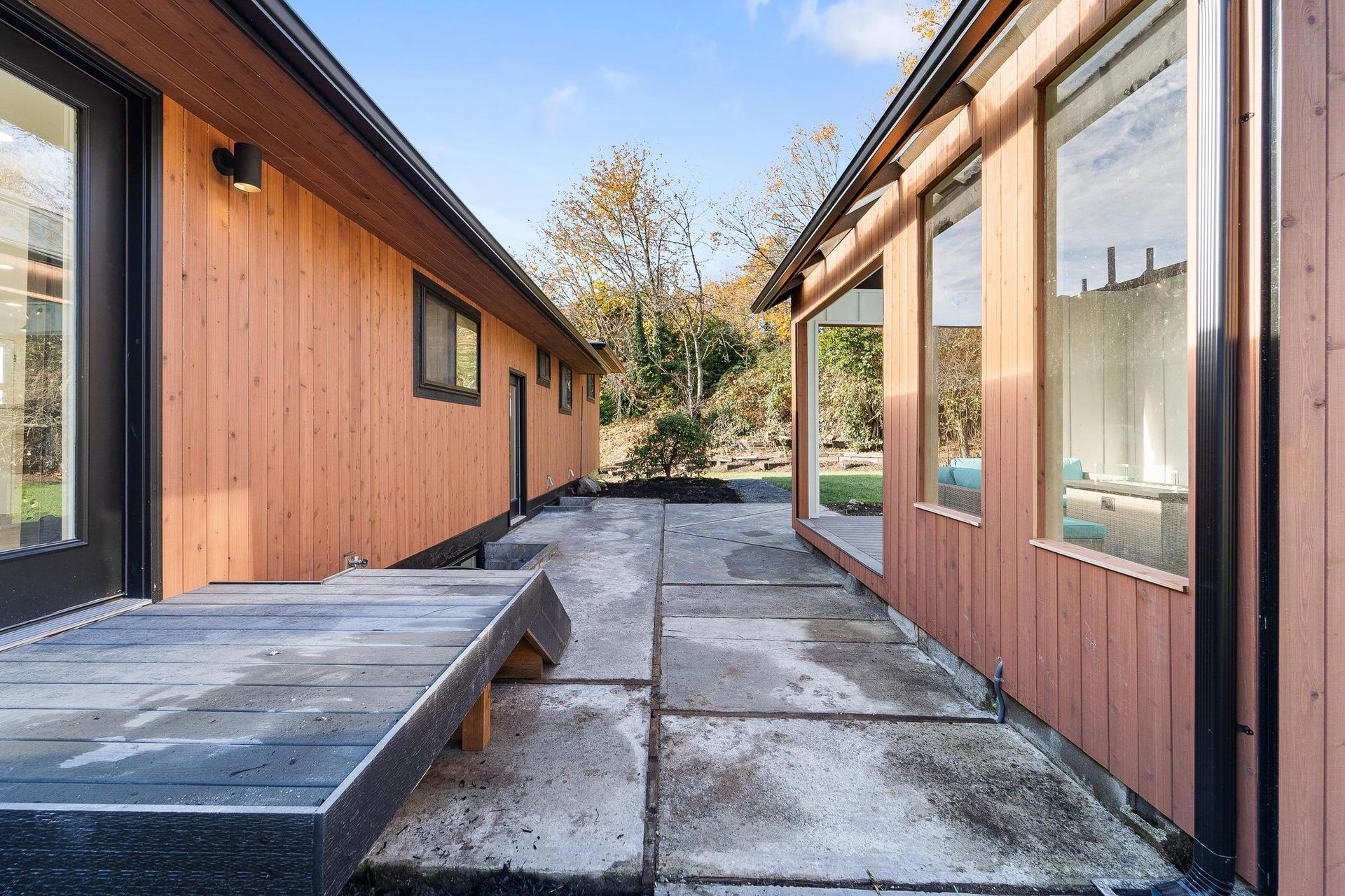 Narrow courtyard between two wooden buildings, with a concrete path and bench in bright daylight