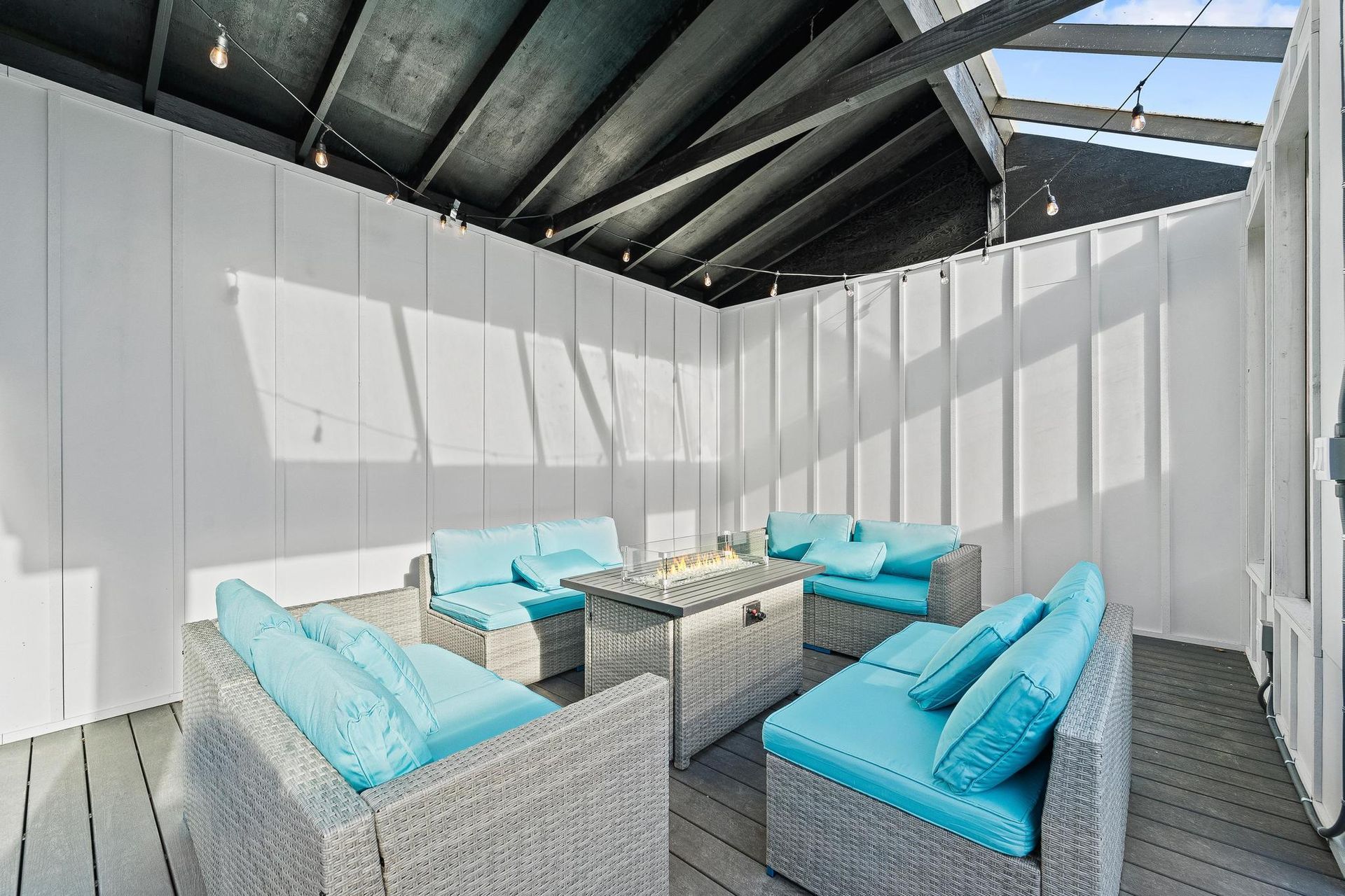 White rooftop patio with light blue cushioned wicker seating and a small table under a metal pergola.