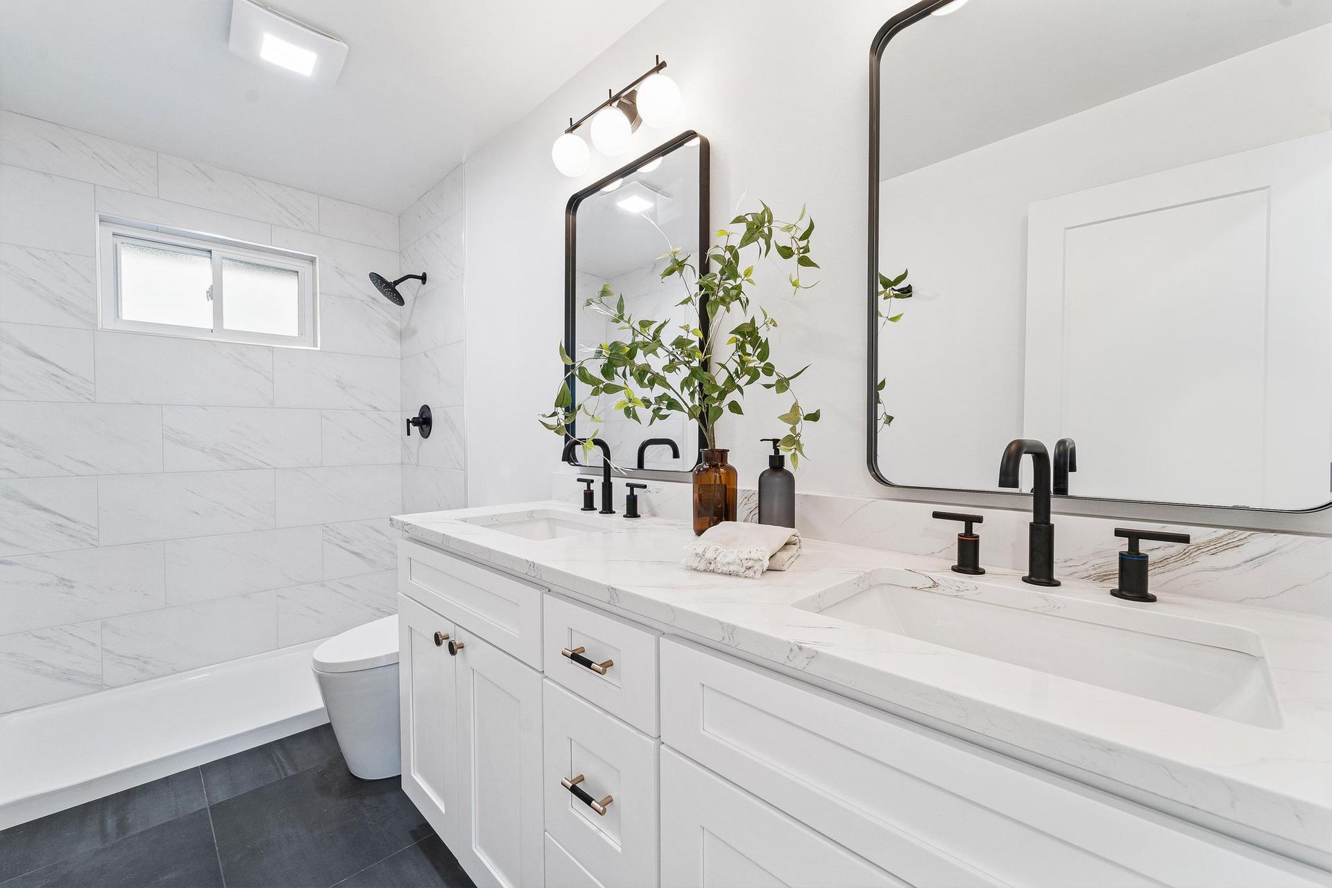 Bright white bathroom with double vanity, black fixtures, large mirror, and tiled tub area