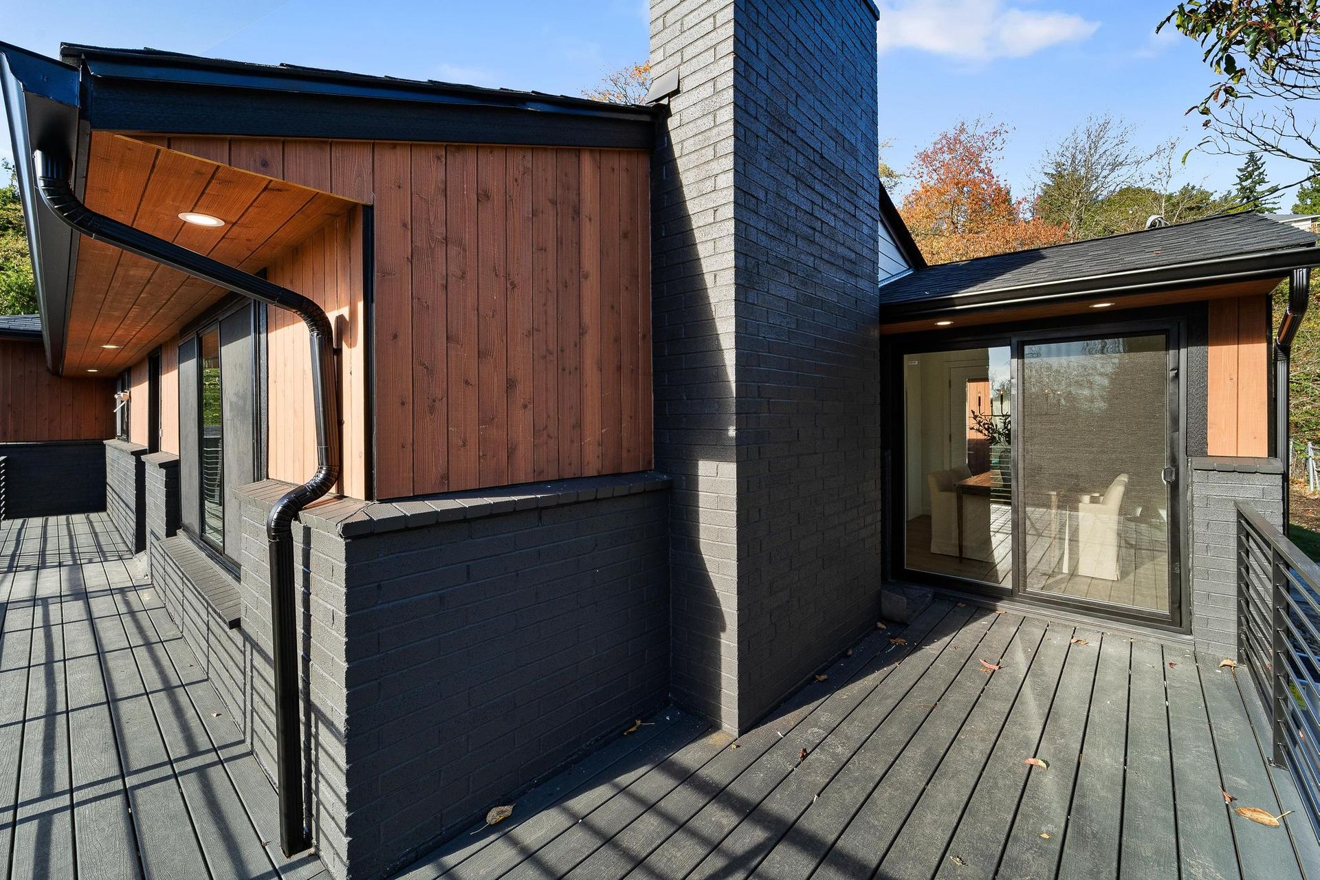 Modern courtyard with dark wood siding, brick chimney, and large glass doors on a paved deck.