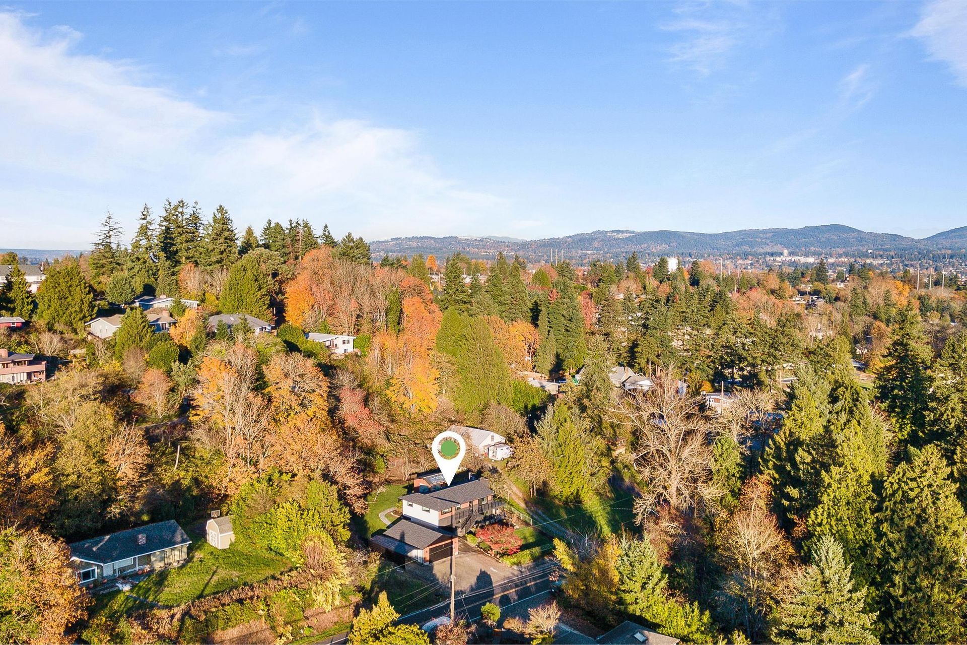 Aerial view of a tree-covered neighborhood with autumn foliage and distant hills under a clear sky