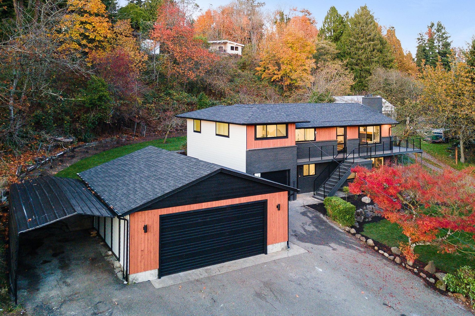 Modern two-story house with black garage, surrounded by autumn trees and a driveway