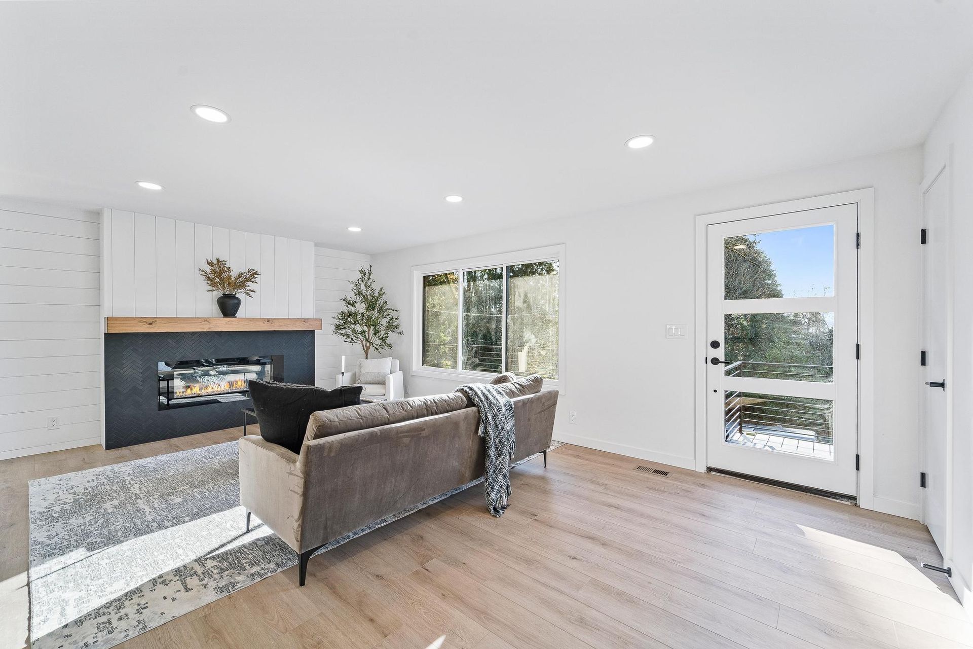 Bright living room with gray sofa, fireplace, large windows, and light wood floors
