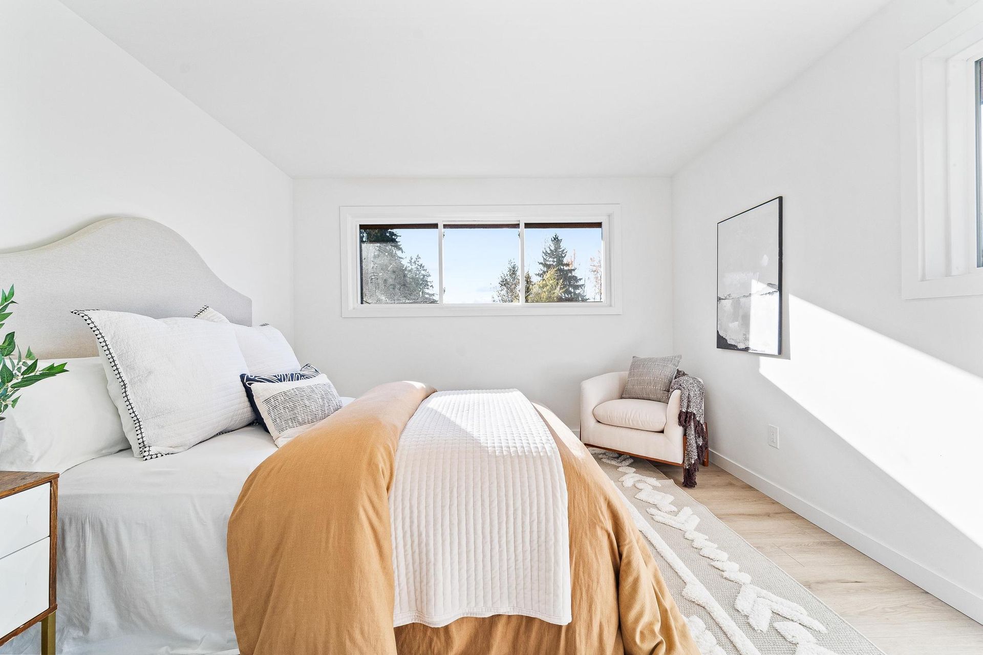 Bright white bedroom with a bed, window, armchair, and a sloped ceiling