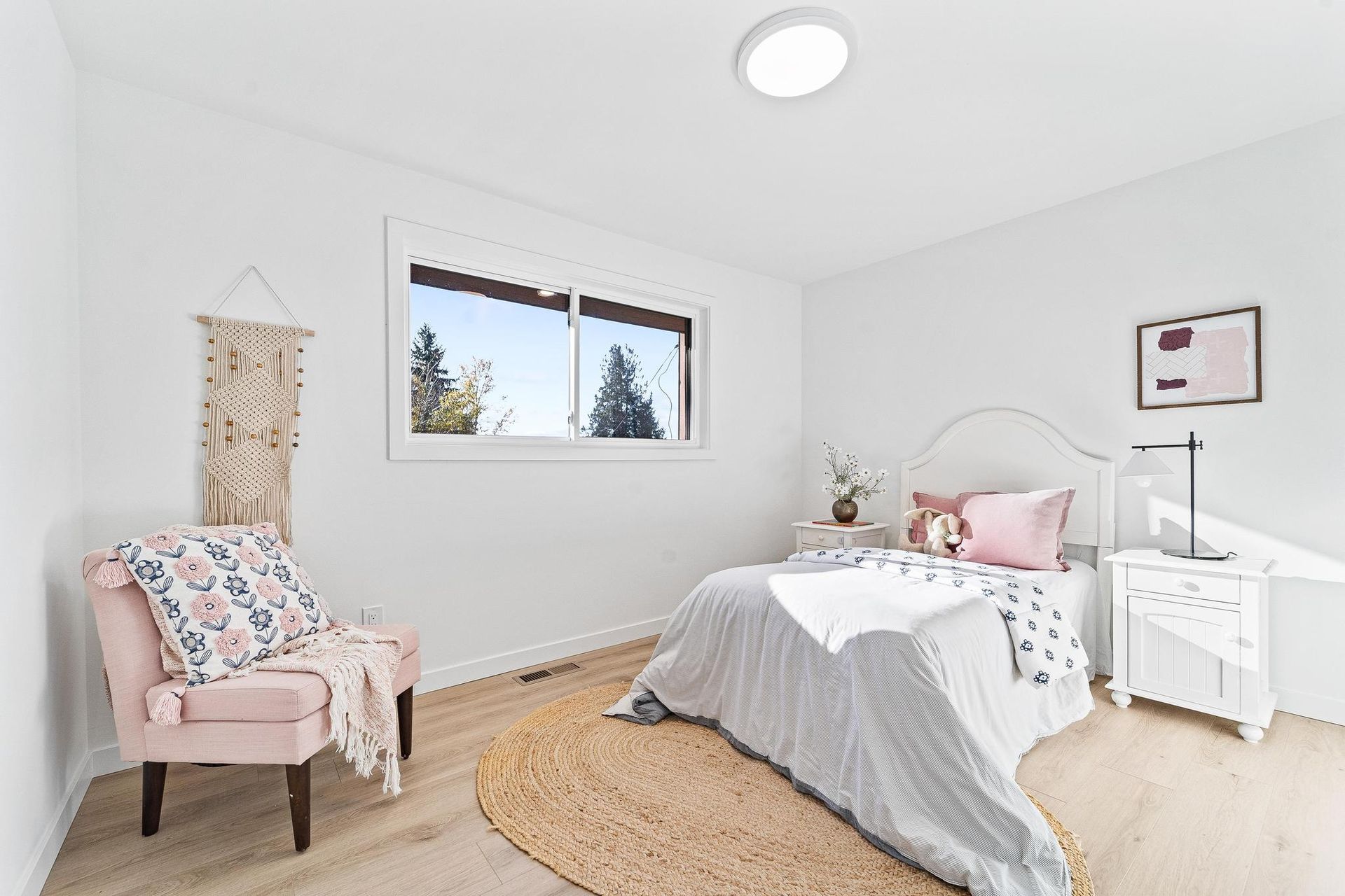 Bright minimalist bedroom with white bed, pink chair, dresser, and window light