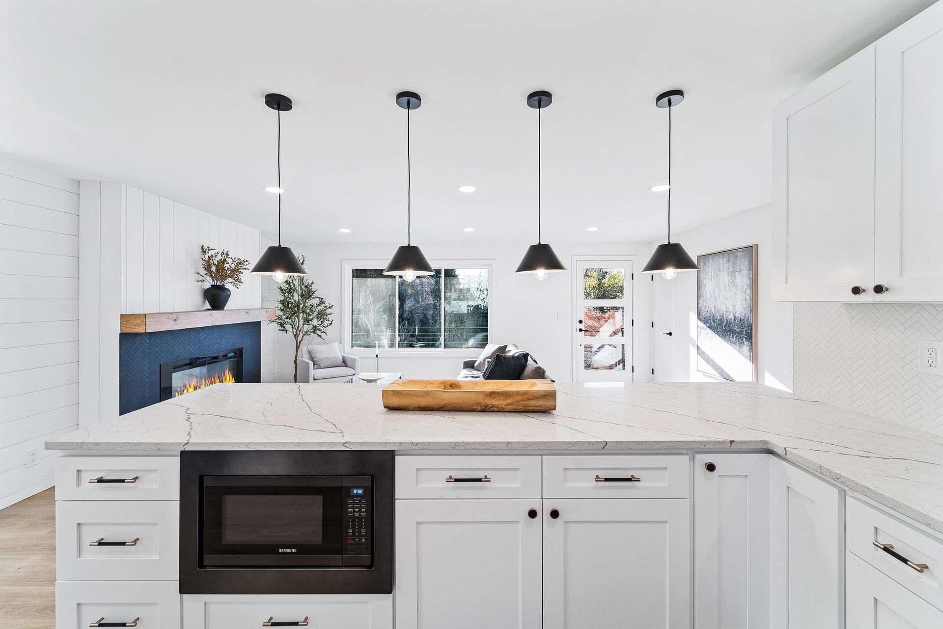 Bright white modern kitchen with island, pendant lights, built-in oven, and large window by the sink