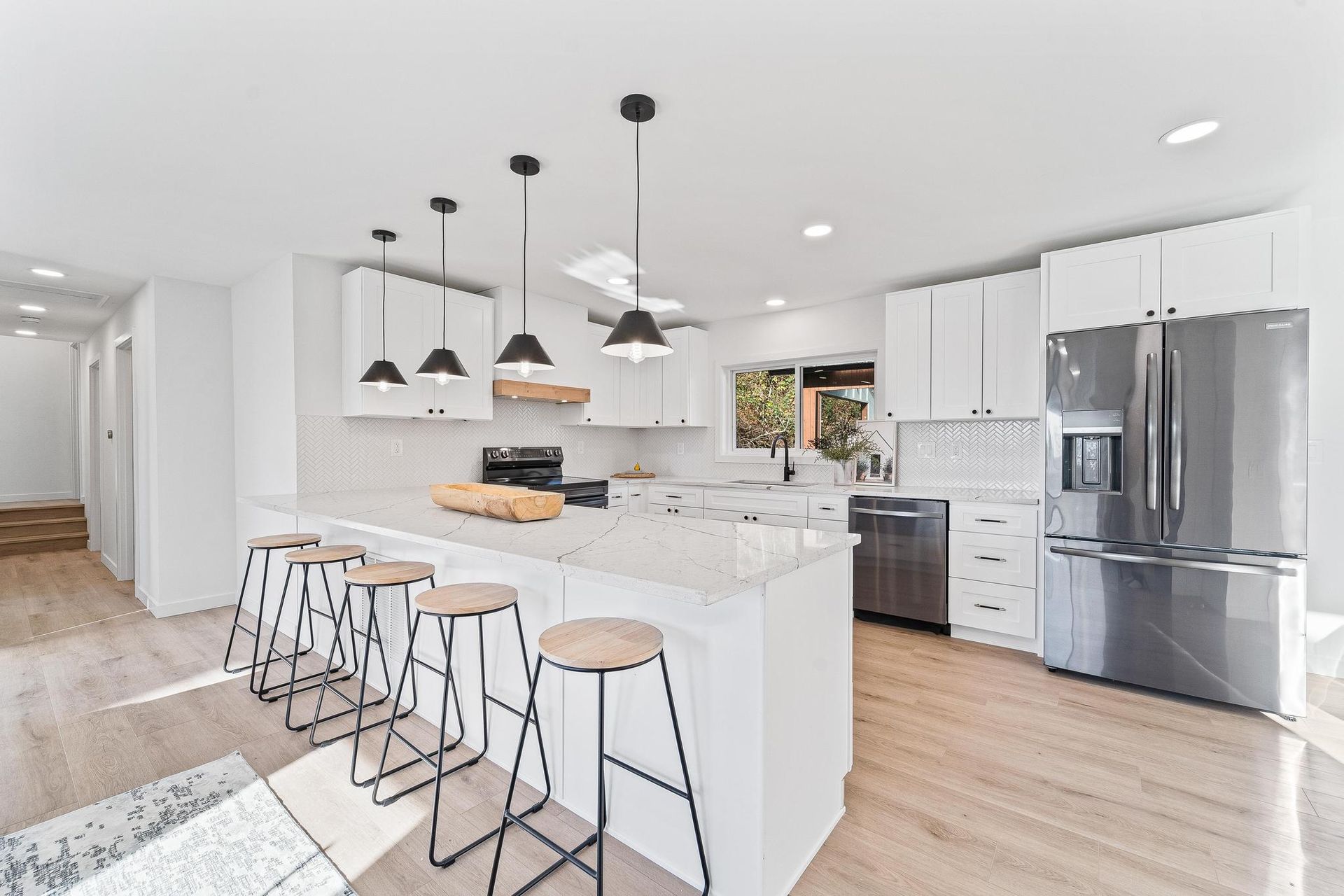 Bright modern kitchen with white cabinets, island seating, pendant lights, and stainless steel appliances