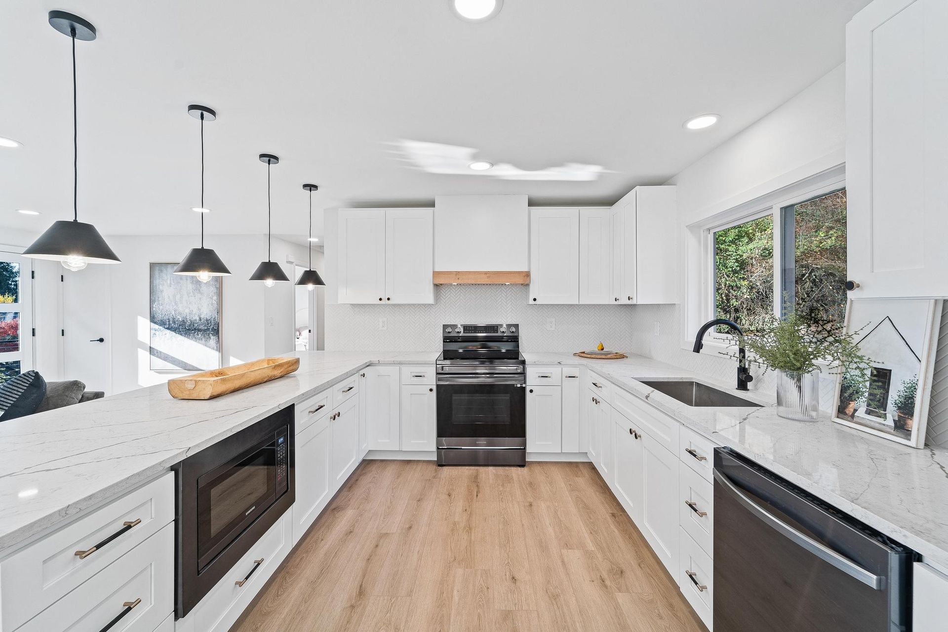 Bright white modern kitchen with island, black pendant lights, stainless appliances, and wood floor.