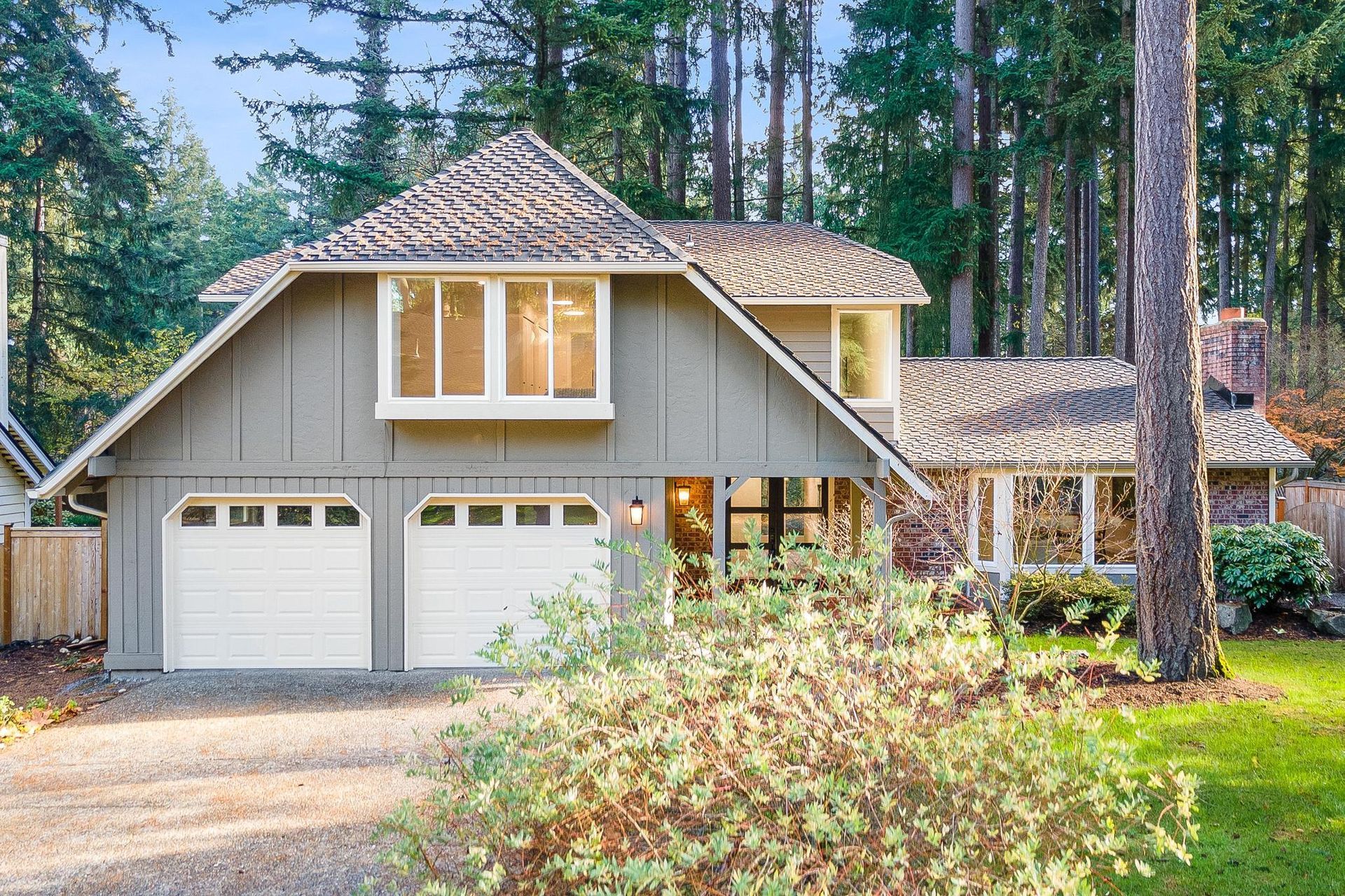 Suburban two-story house with two-car garage, beige siding, and tall trees in front yard