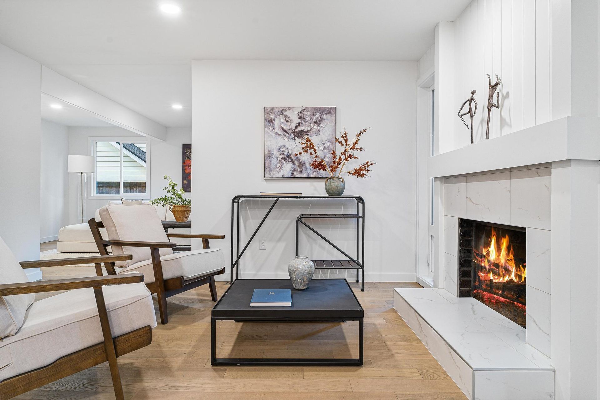 Bright modern living room with white walls, black coffee table, and a lit fireplace.