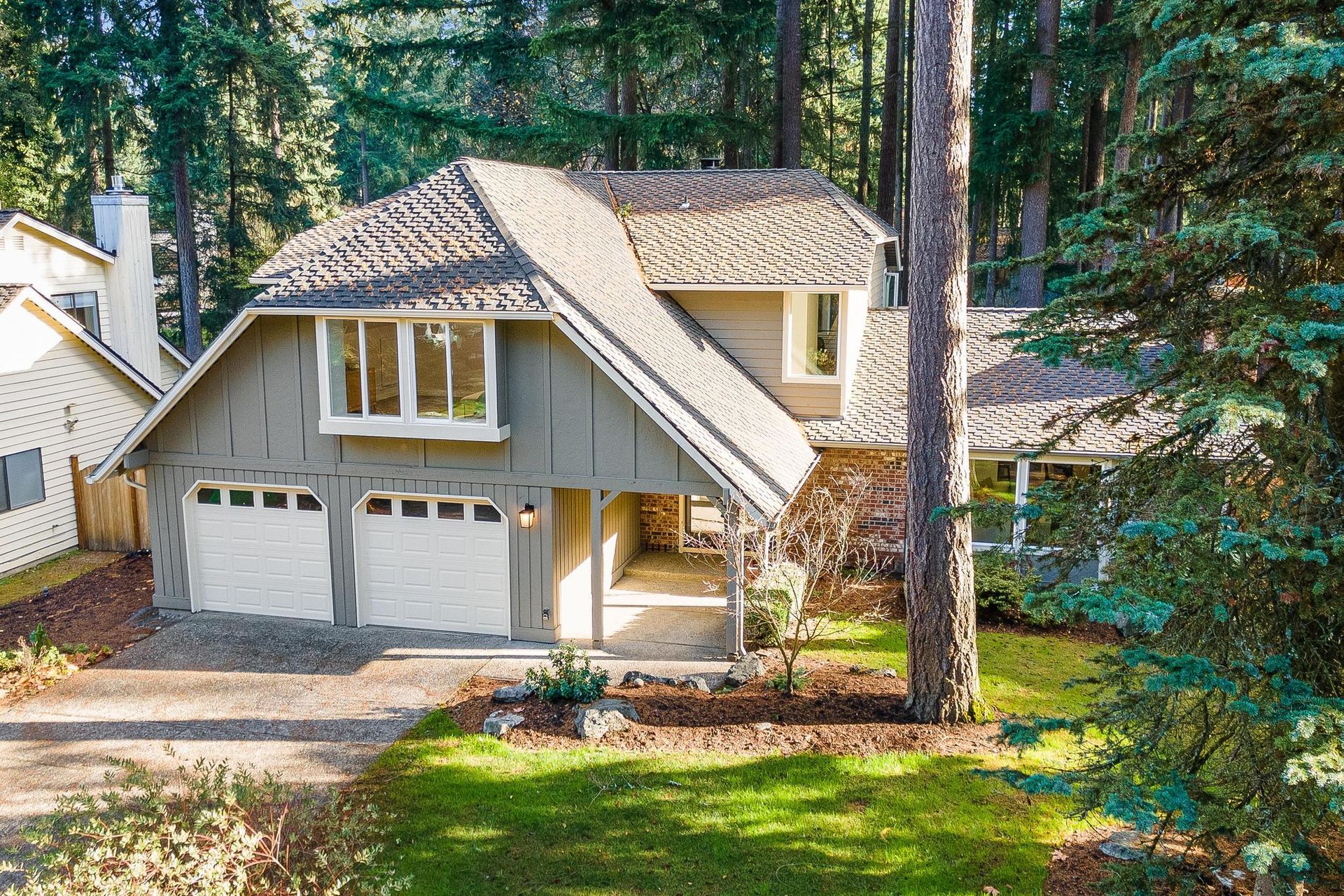 Suburban house with beige siding, two-car garage, and tall pine trees in the yard