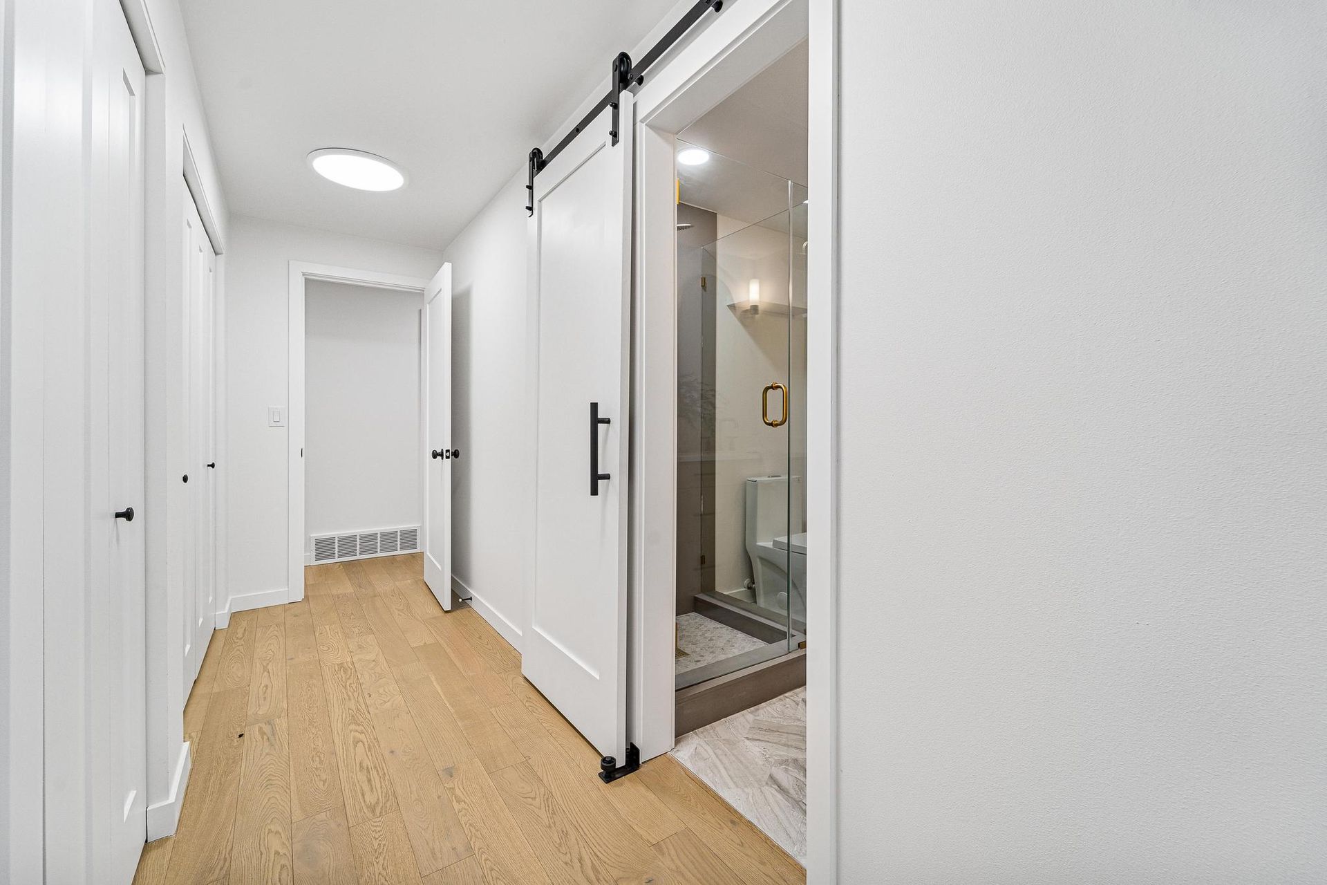 Bright hallway with white walls, wood floor, and a sliding bathroom door open on the right.