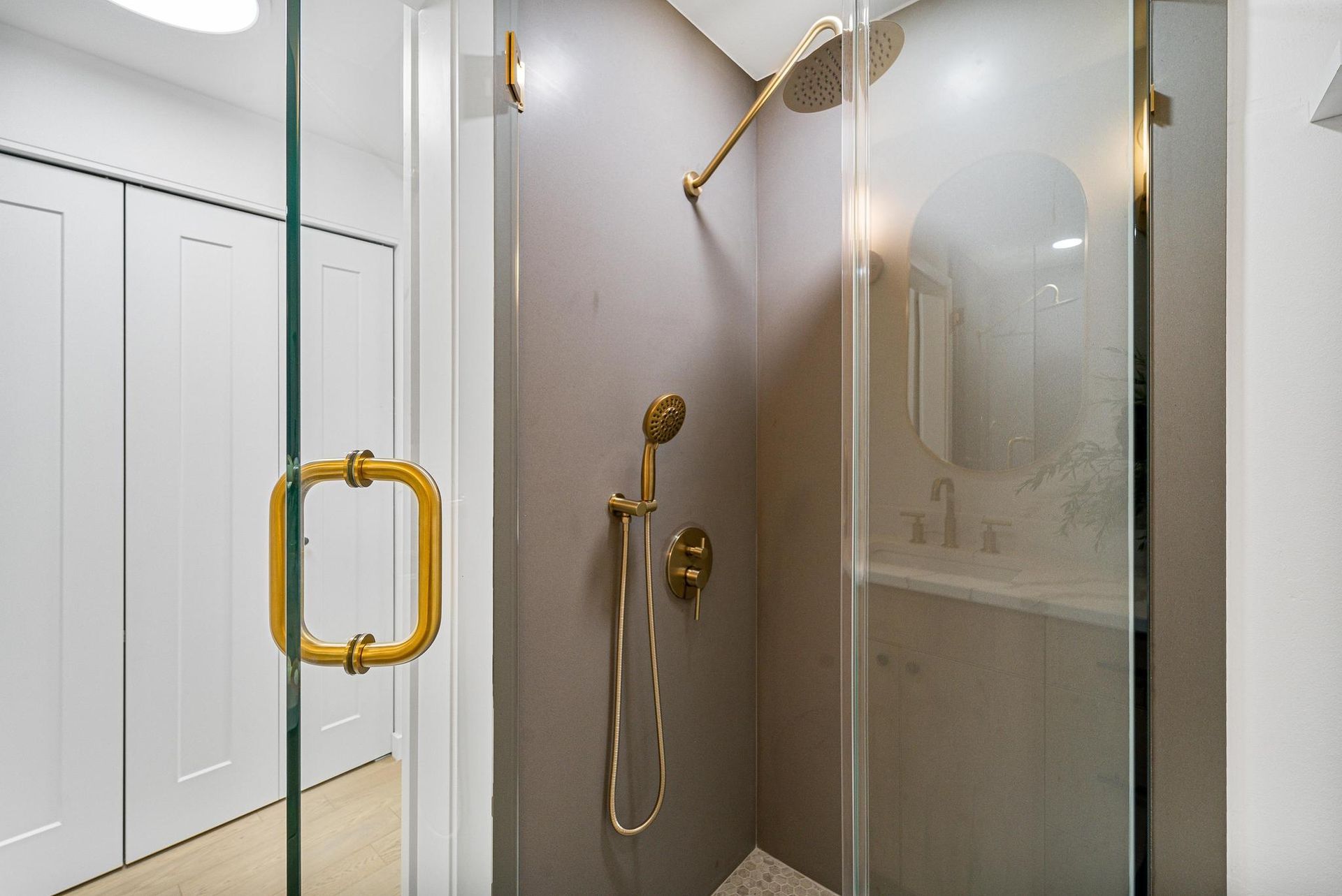 Glass shower stall with gold fixtures and a white bathroom vanity in the background