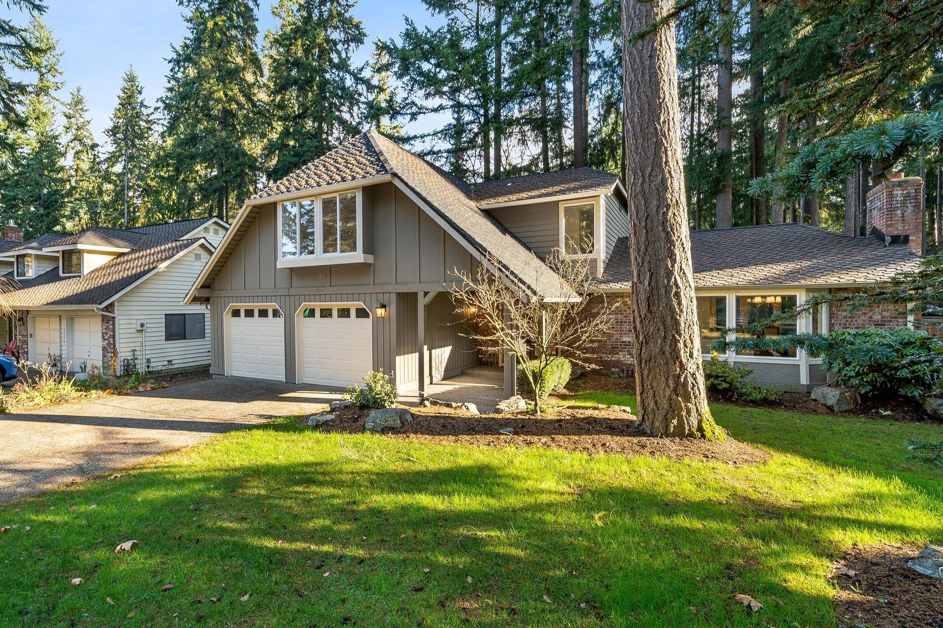 Two-story beige house with a garage, tall trees, and a green front lawn