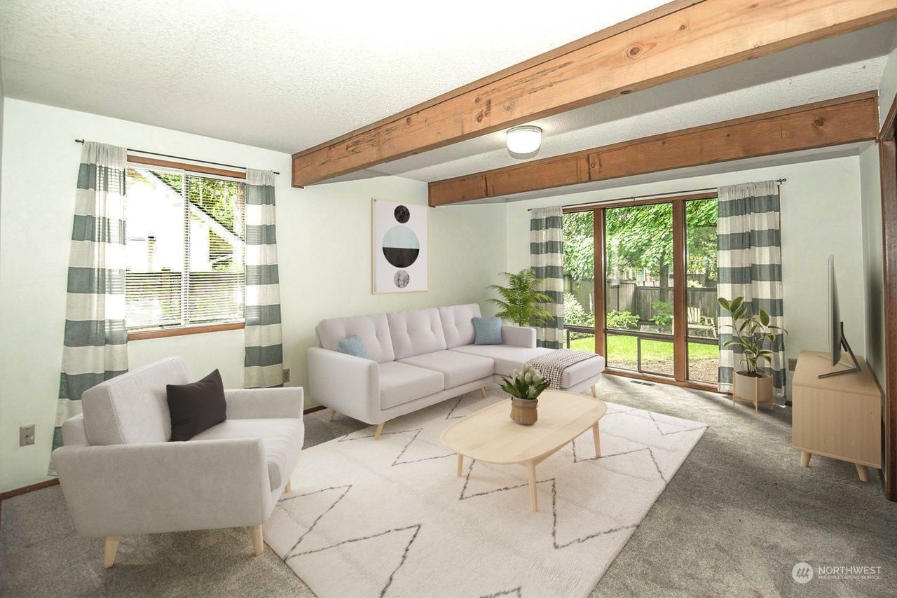 Bright modern living room with white sofas, wood beam ceiling, and large windows overlooking greenery