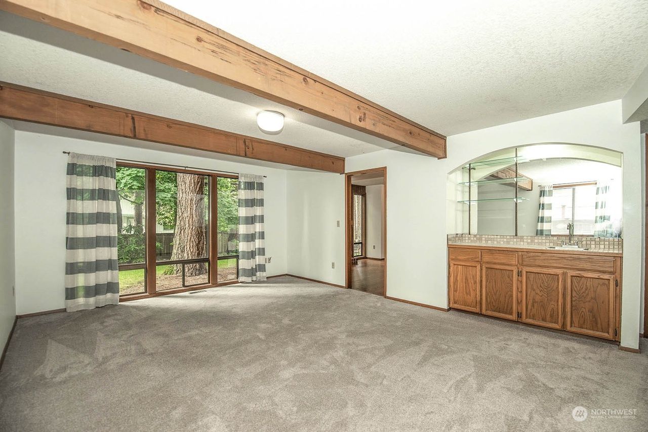 Empty living room with vaulted wood beam ceiling, sliding glass door, and wooden sideboard with mirror.