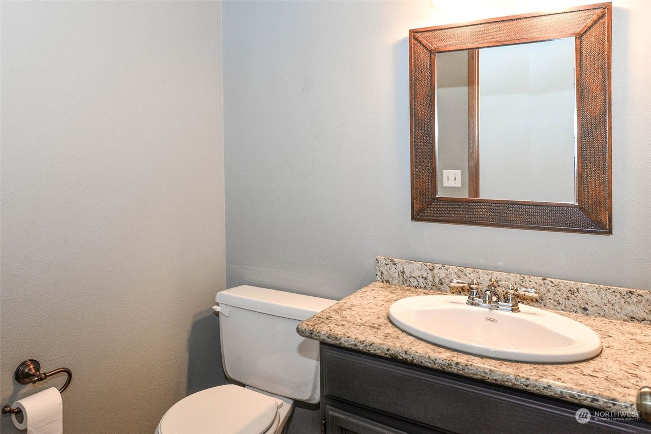 Small bathroom with toilet, sink, granite countertop, and framed mirror above the vanity.
