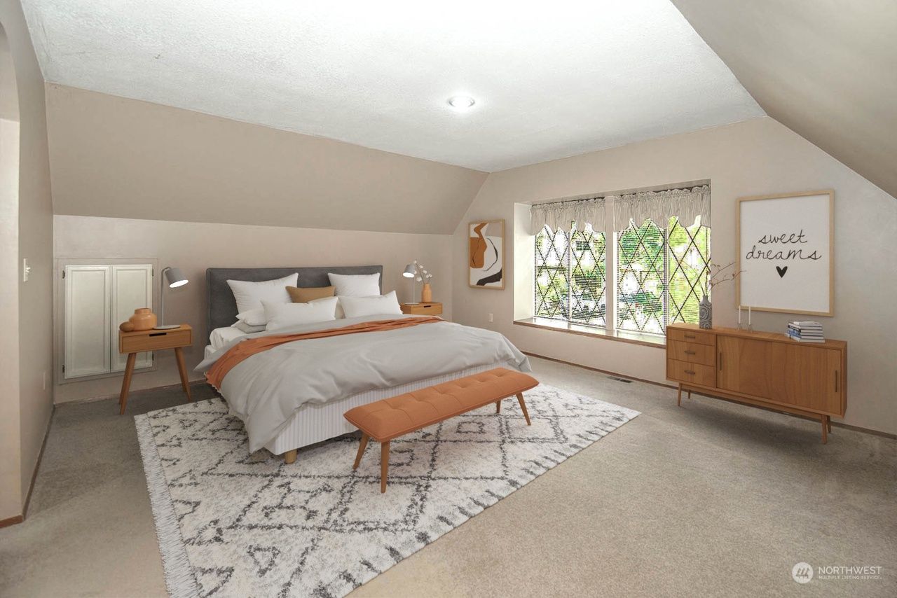 Cozy beige bedroom with a large bed, patterned rug, wooden dresser, and bright window seating area.