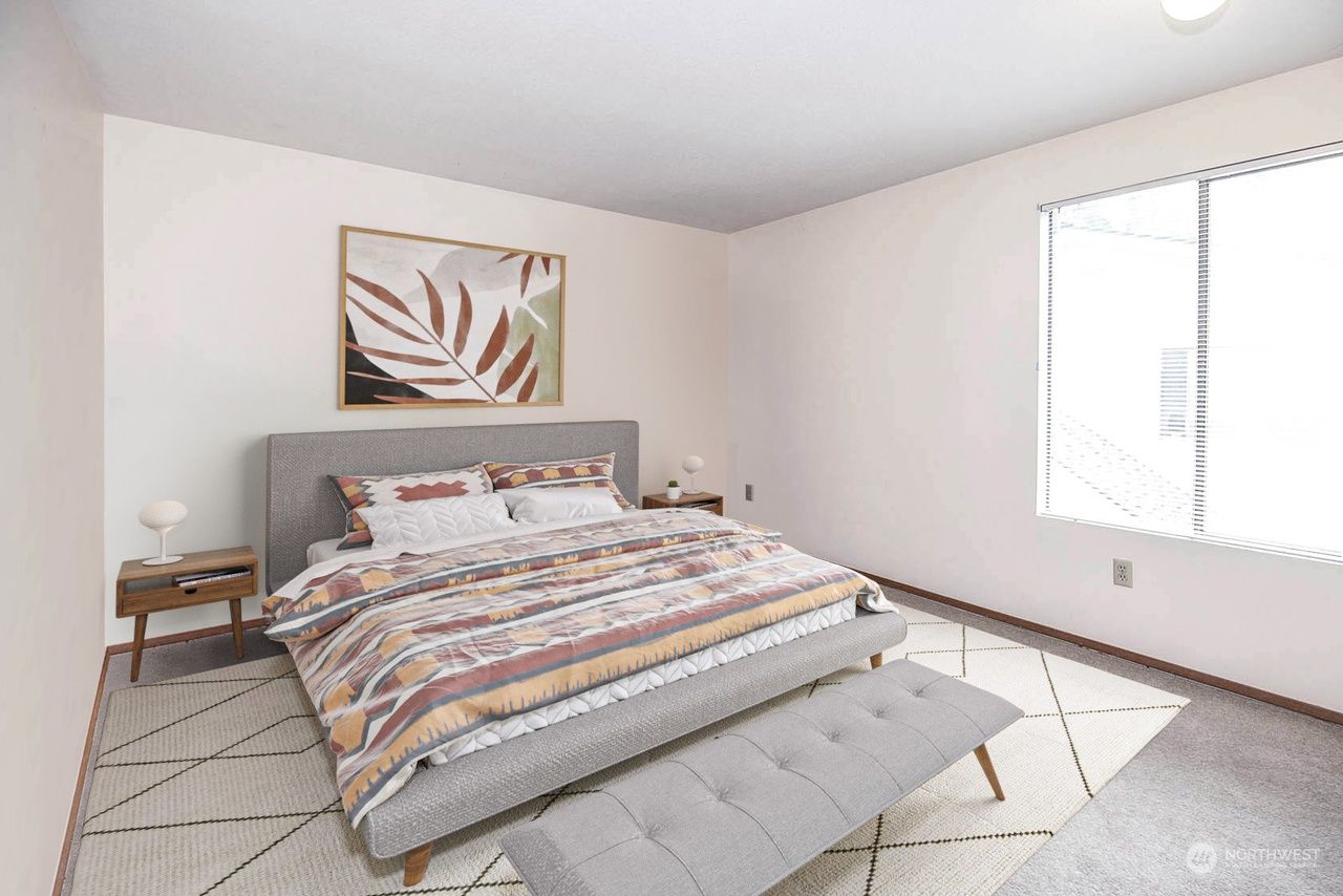 Bright bedroom with a bed, patterned bedding, gray rug, wall art, and a window letting in daylight.