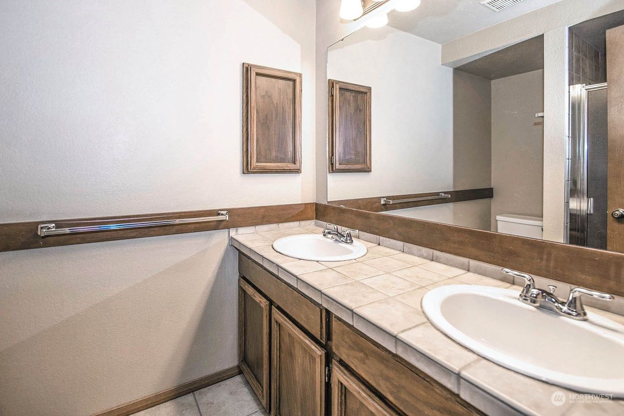 Bathroom vanity with beige countertop, double sinks, large mirror, and wooden cabinets