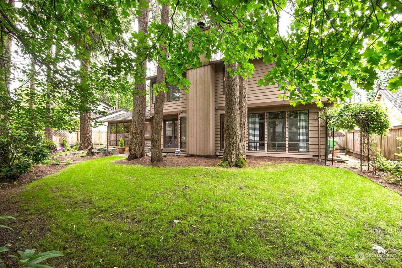 Wooded backyard with a two-story brick house and large green lawn under leafy trees