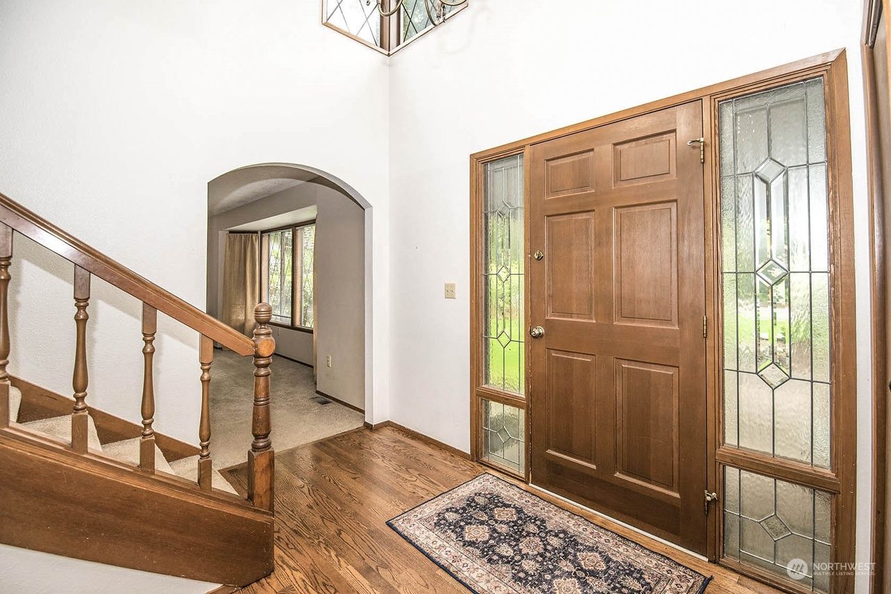 Bright entryway with wooden stairs, front door, rug, and decorative glass panels